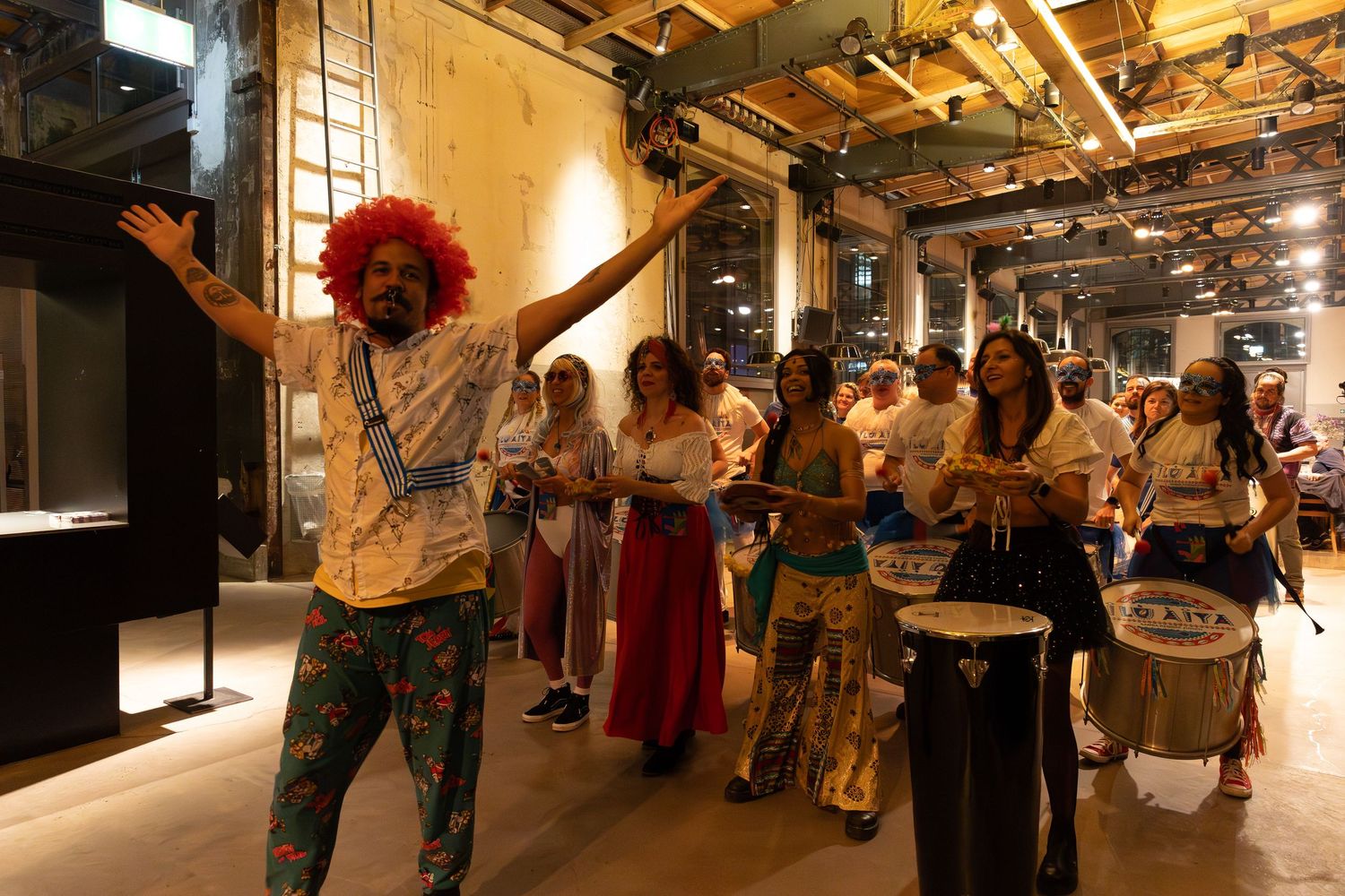 Performers with drums and colorful outfits dance in an indoor venue.