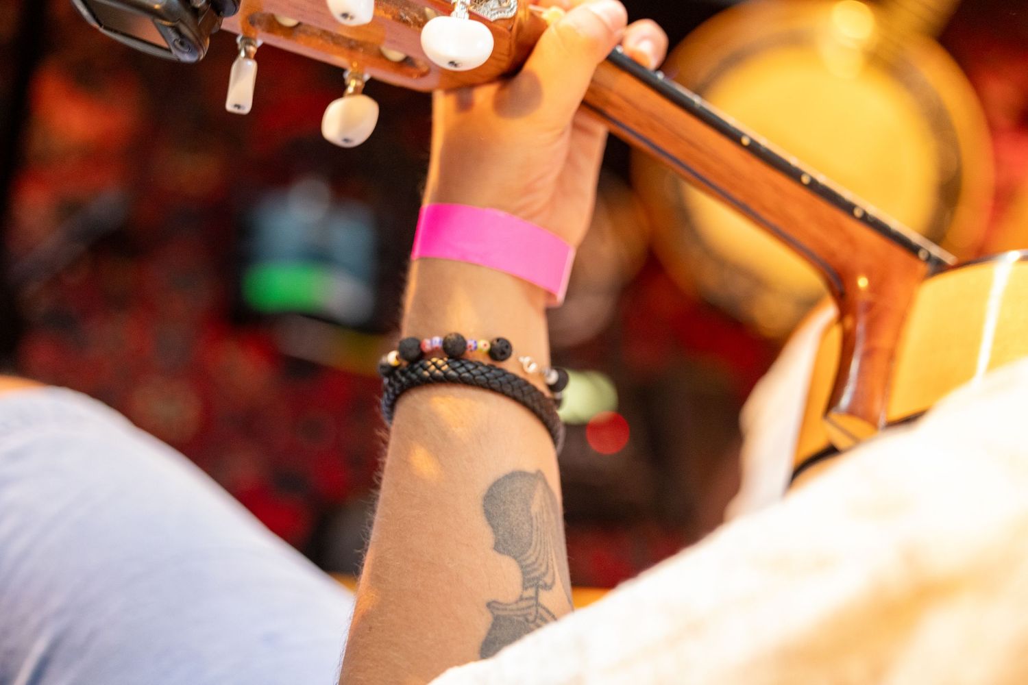 Close-up of hands playing acoustic guitar with visible arm tattoo and jewelry.