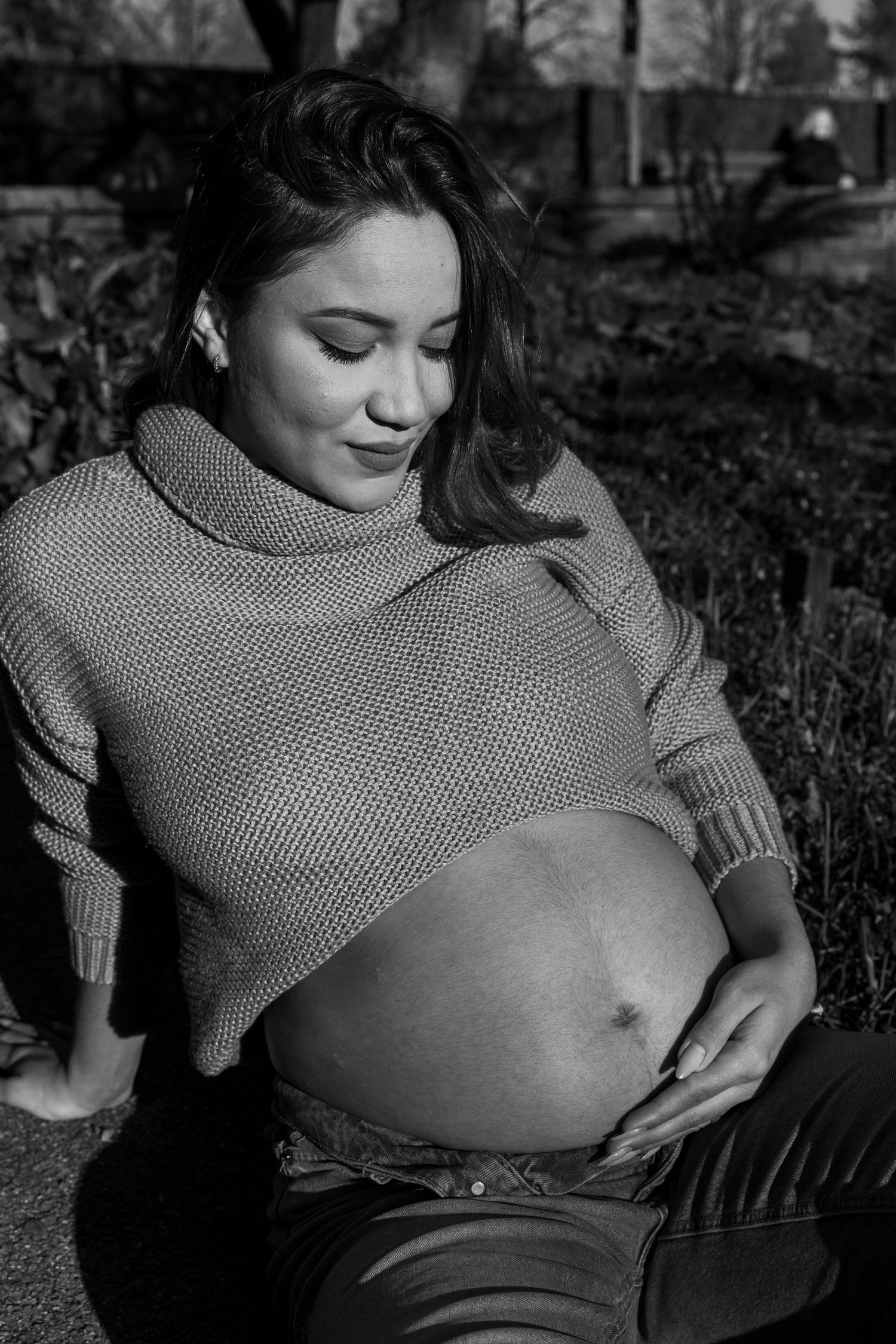 Black and white maternity portrait with woman in knit sweater sitting outdoors.