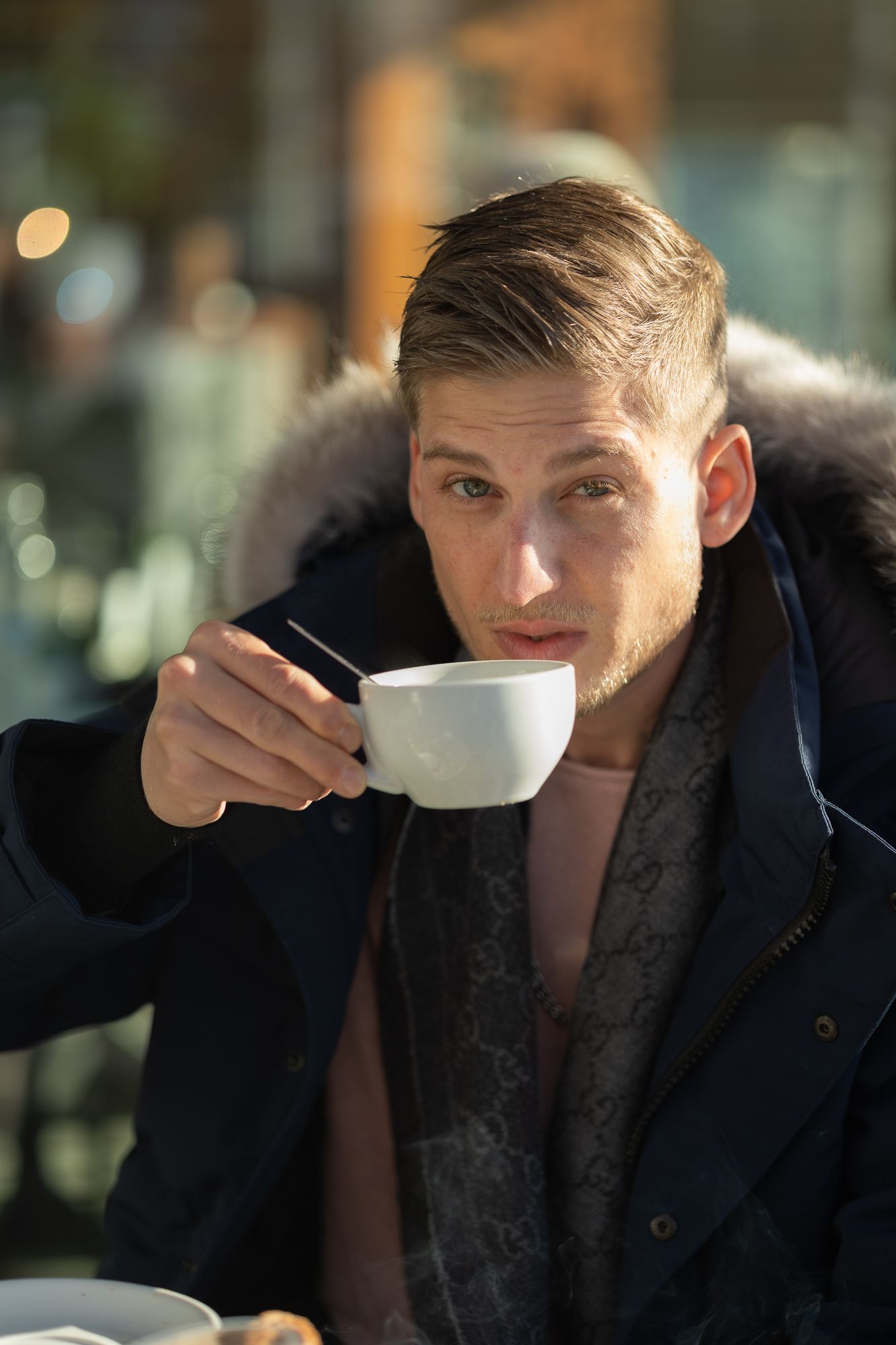 Candid moment captured while drinking from a white coffee cup wearing a navy winter jacket.