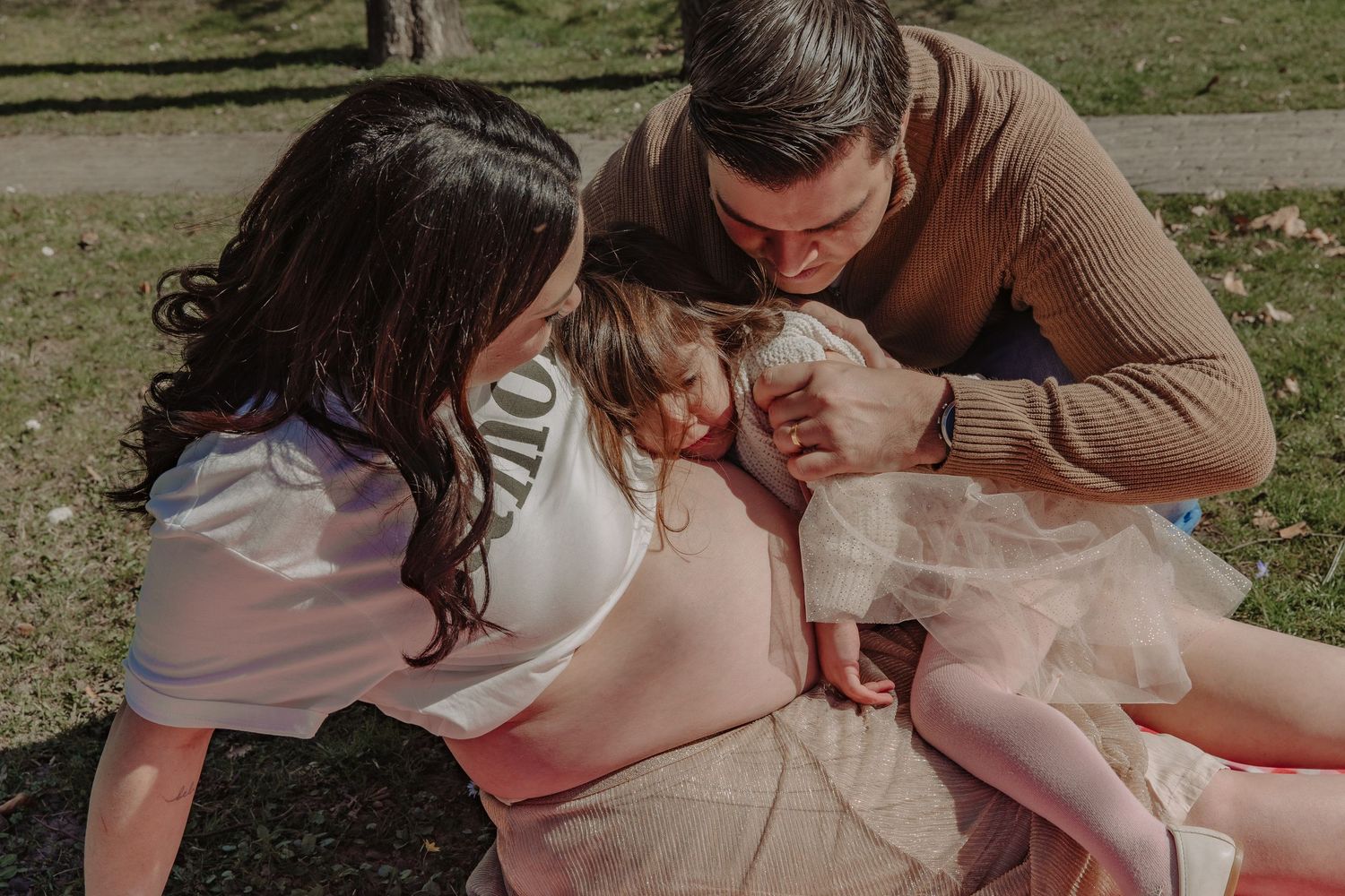 A family shares joyful moments together while lounging on a red picnic blanket in the park.