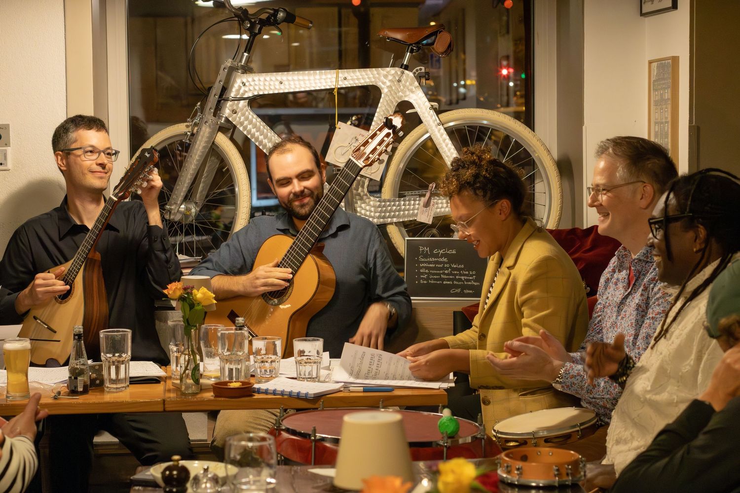 Group of musicians performing with acoustic instruments at casual indoor gathering.