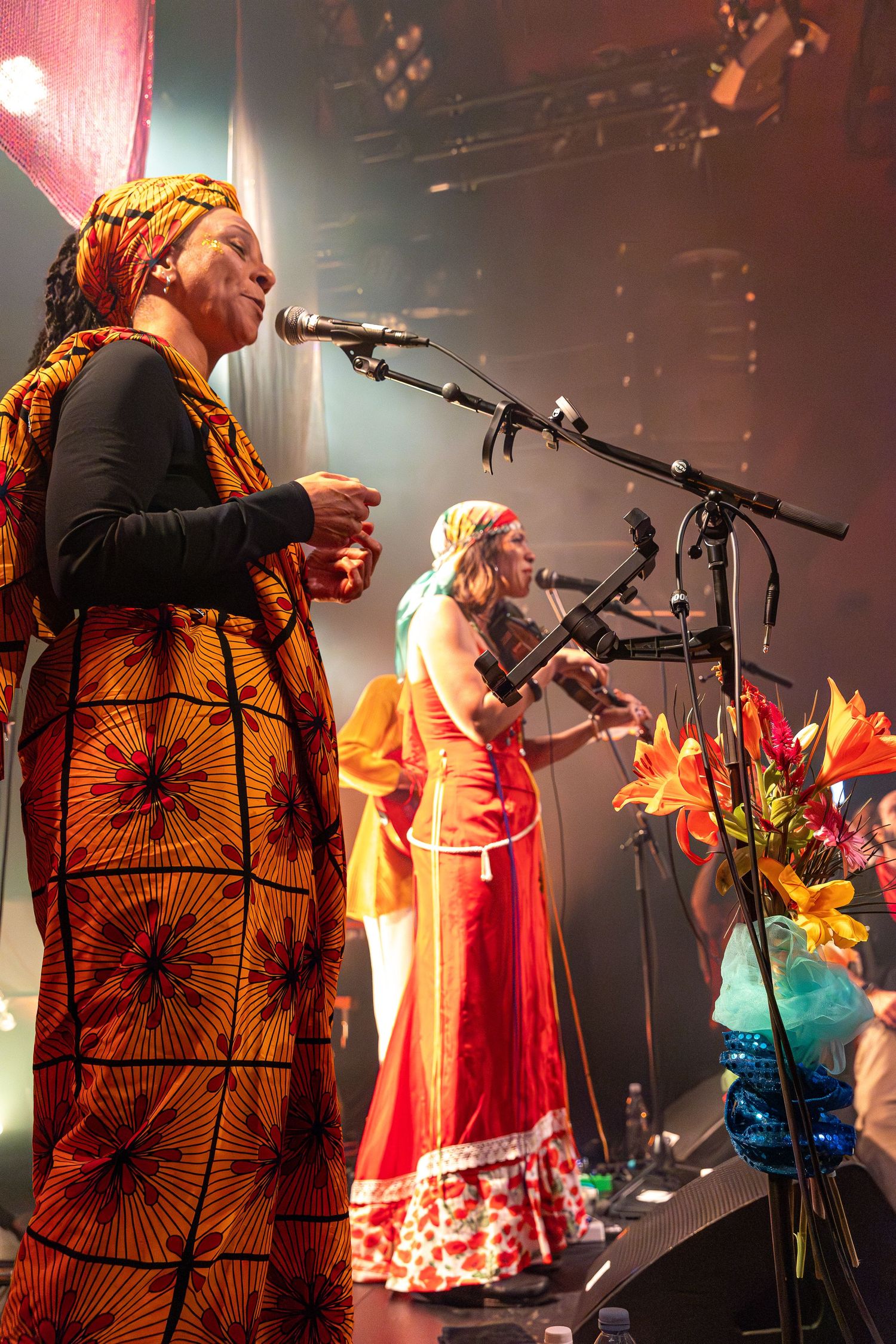 Musicians in colorful attire performing on stage with floral arrangements.
