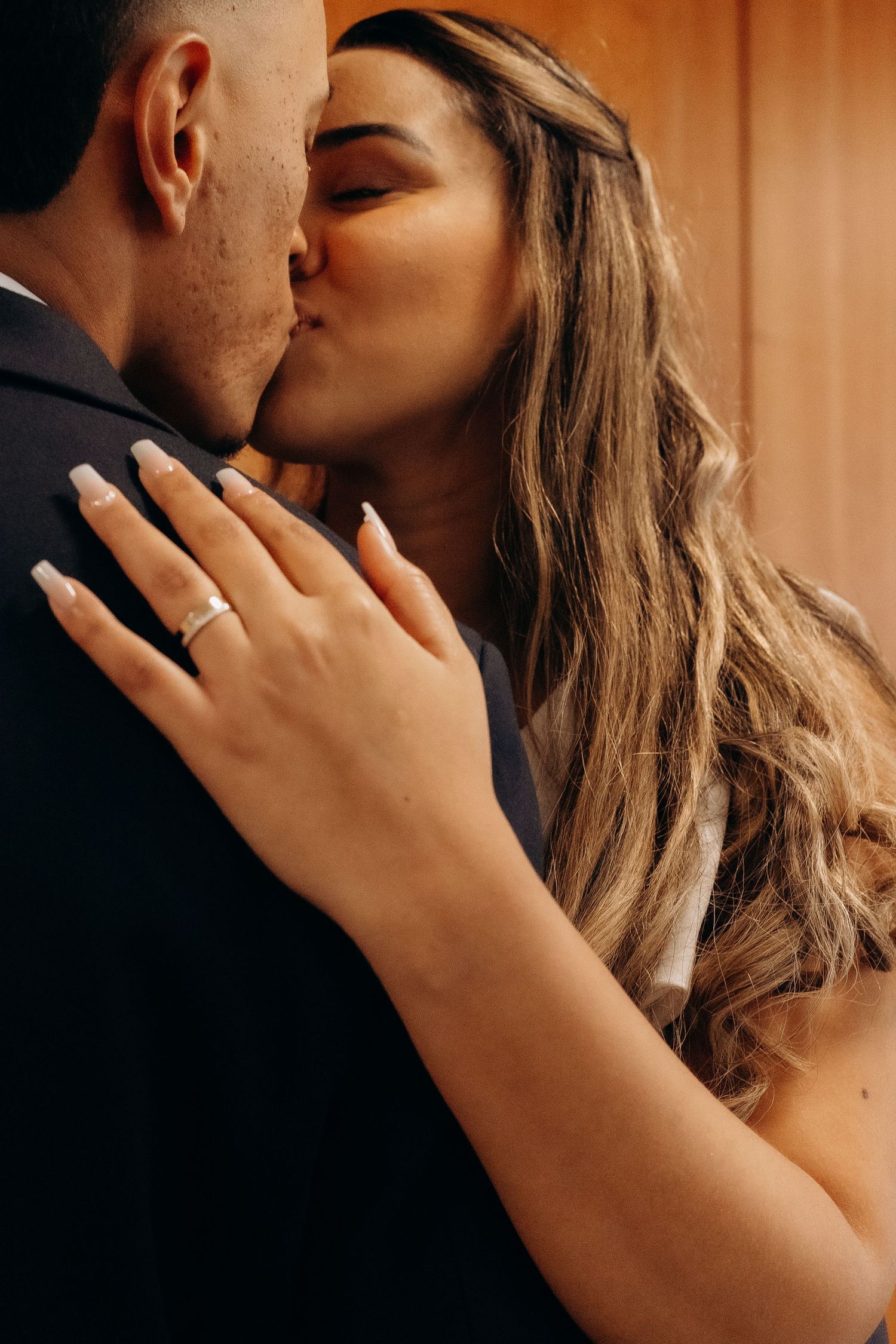 Romantic wedding kiss with ring displayed against wooden backdrop.