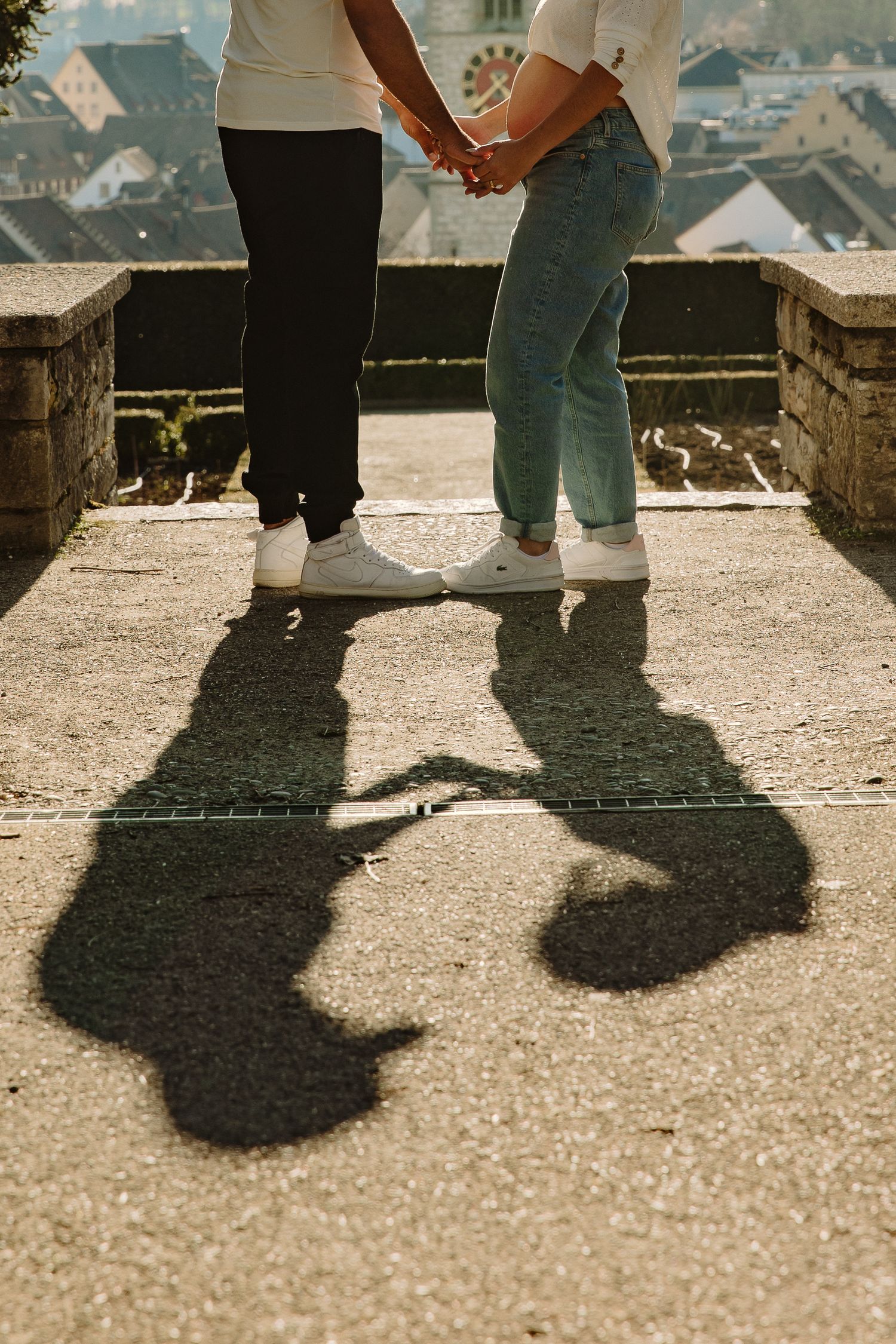 Close-up of couple's feet and shadows while standing together on stone overlook.