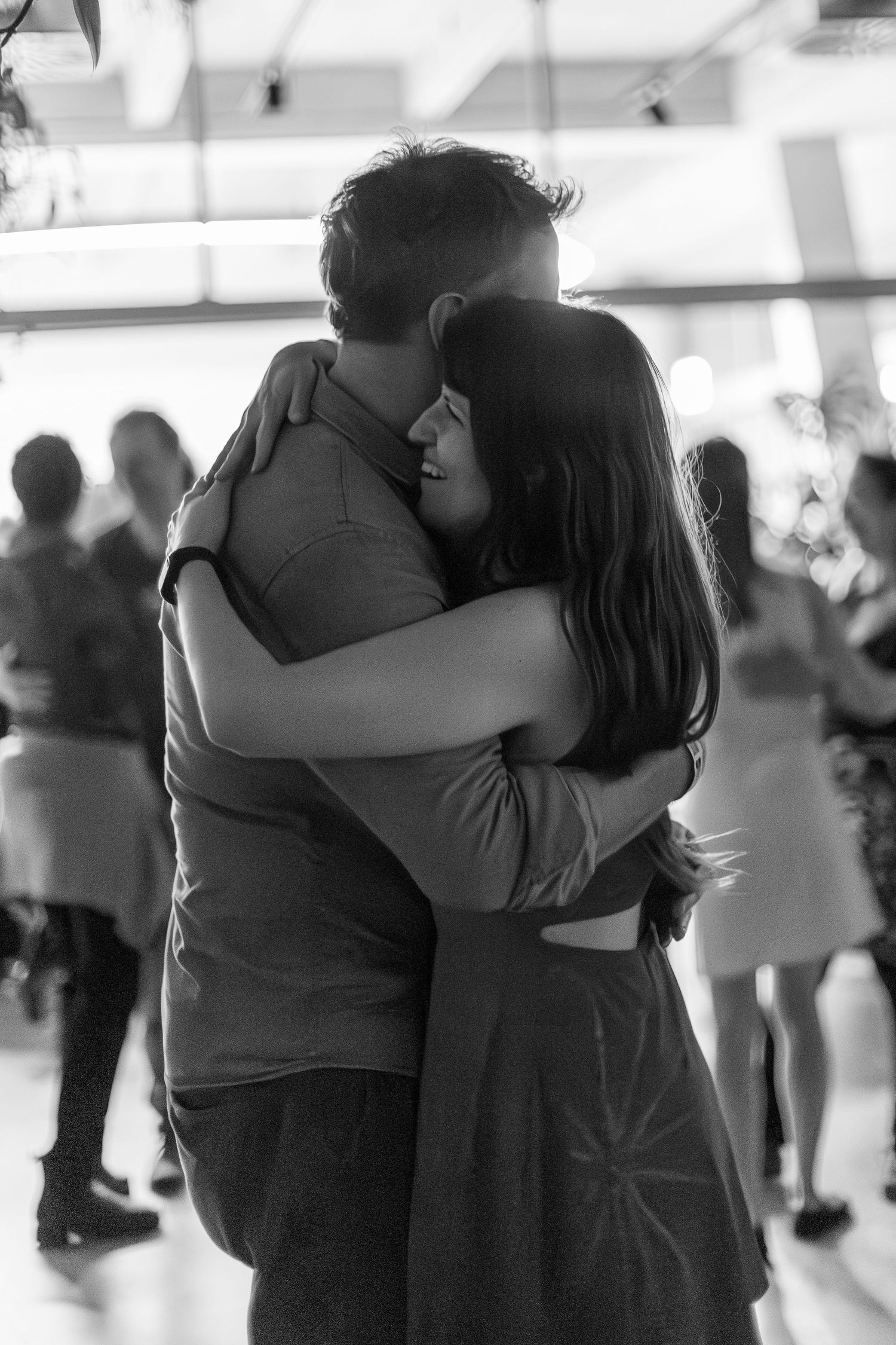 A couple shares a tender dance moment at an indoor event, captured in black and white.