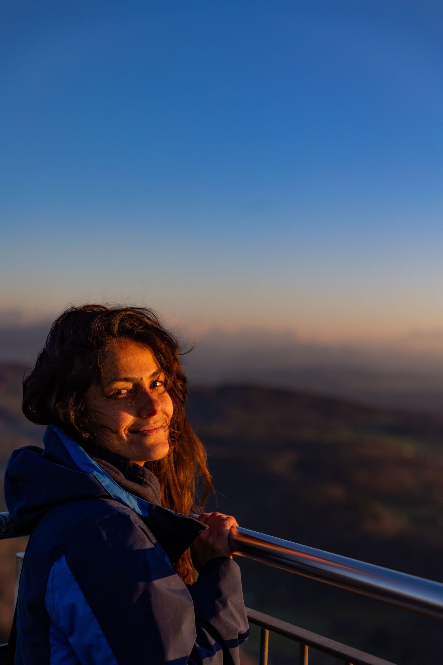 Person in blue jacket illuminated by golden hour light at mountain viewpoint.