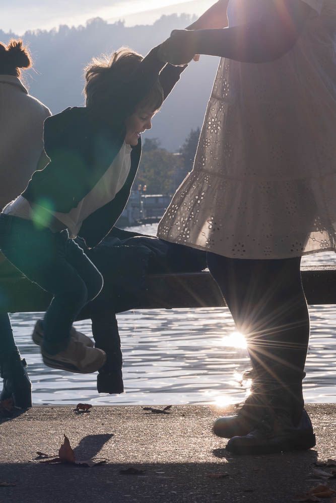 Silhouettes of people playing in backlit sunlight near water during golden hour.