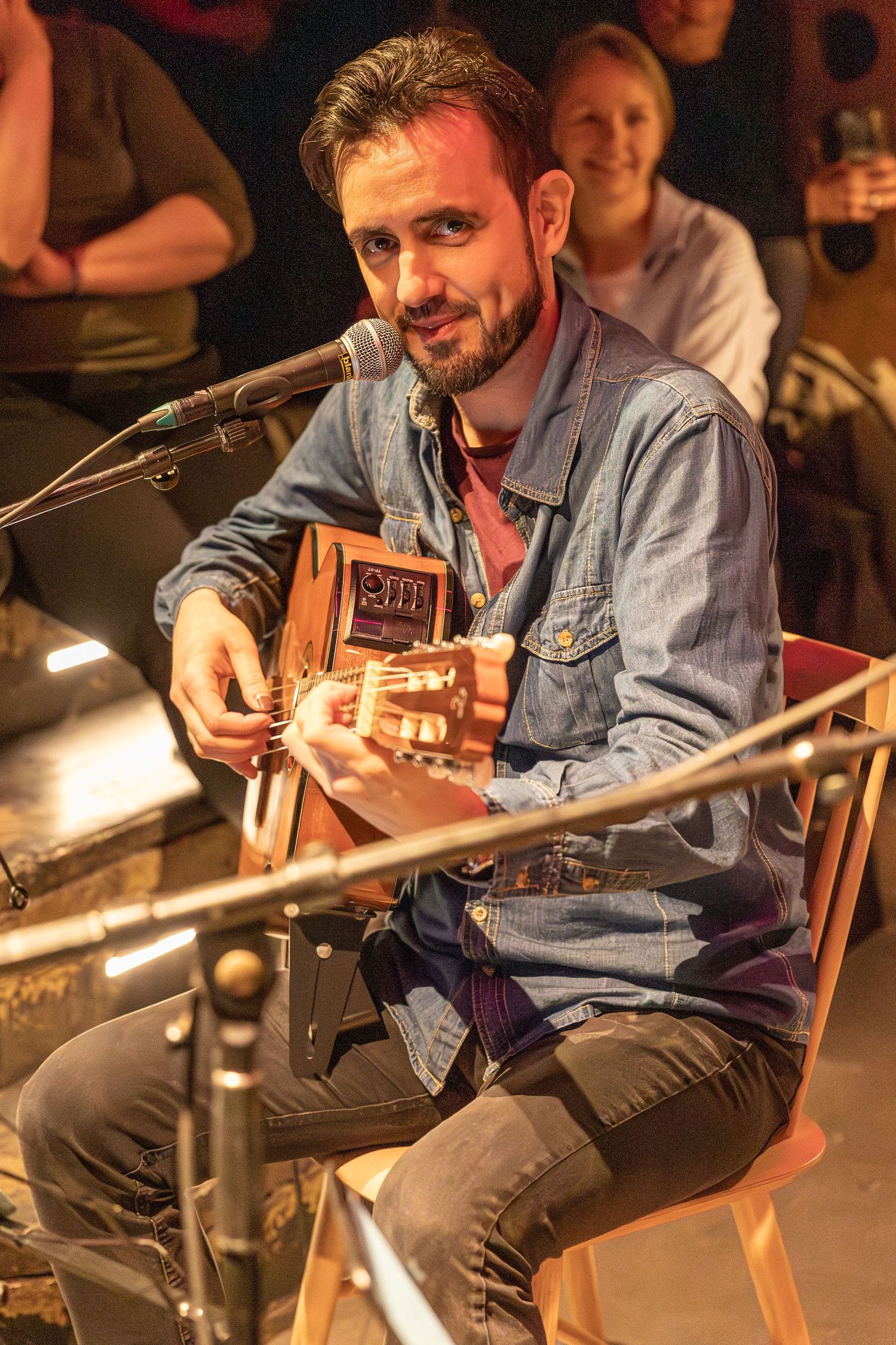 Musician performing with acoustic guitar on stage under warm lighting.
