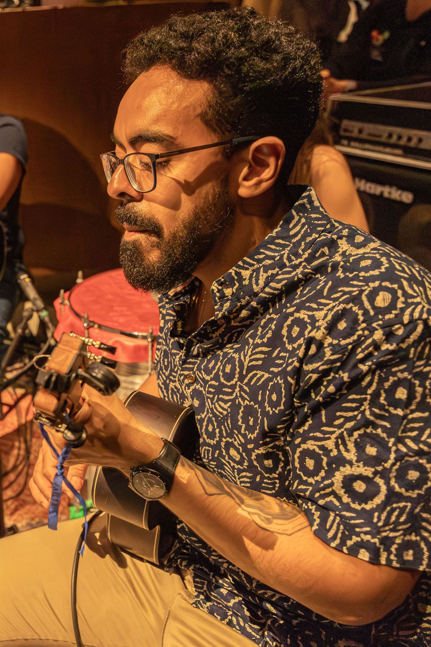 Musician in patterned shirt playing acoustic guitar at intimate venue.