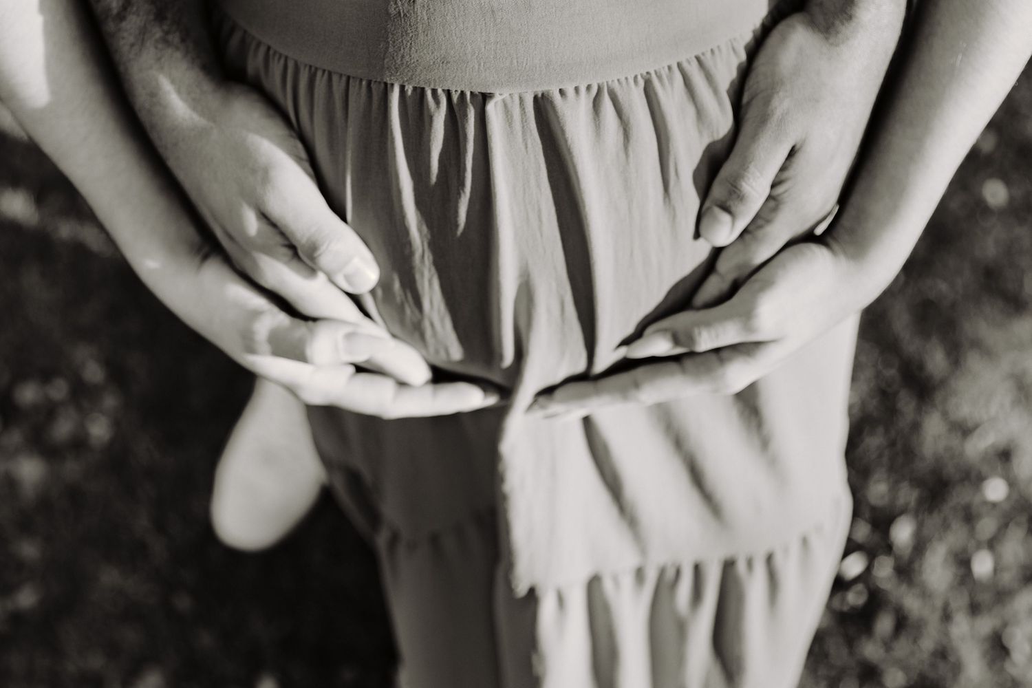 Close-up black and white photo showing hands resting on a gathered dress fabric.