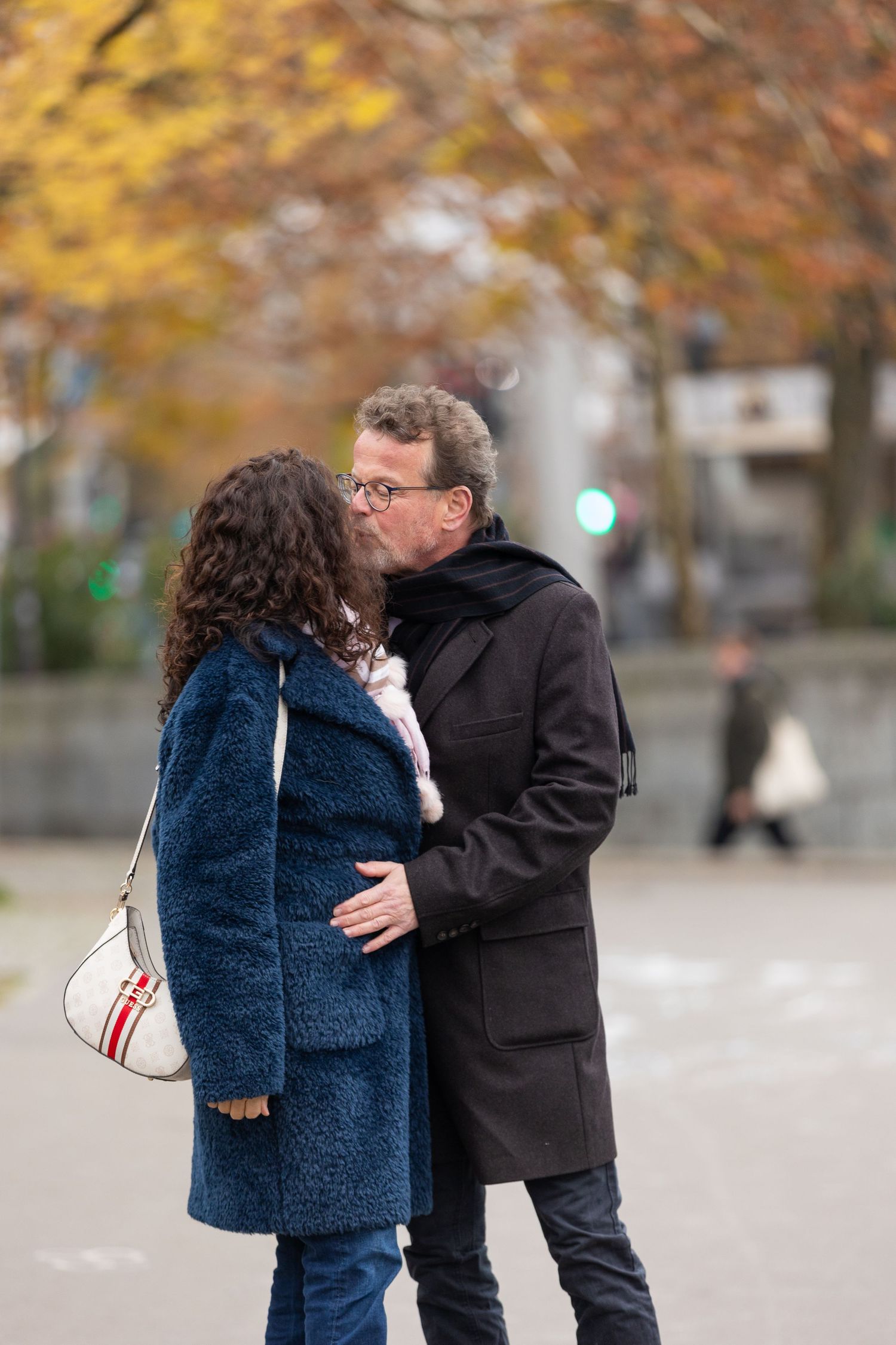 A romantic couple embracing outdoors wearing winter coats on an autumn day.