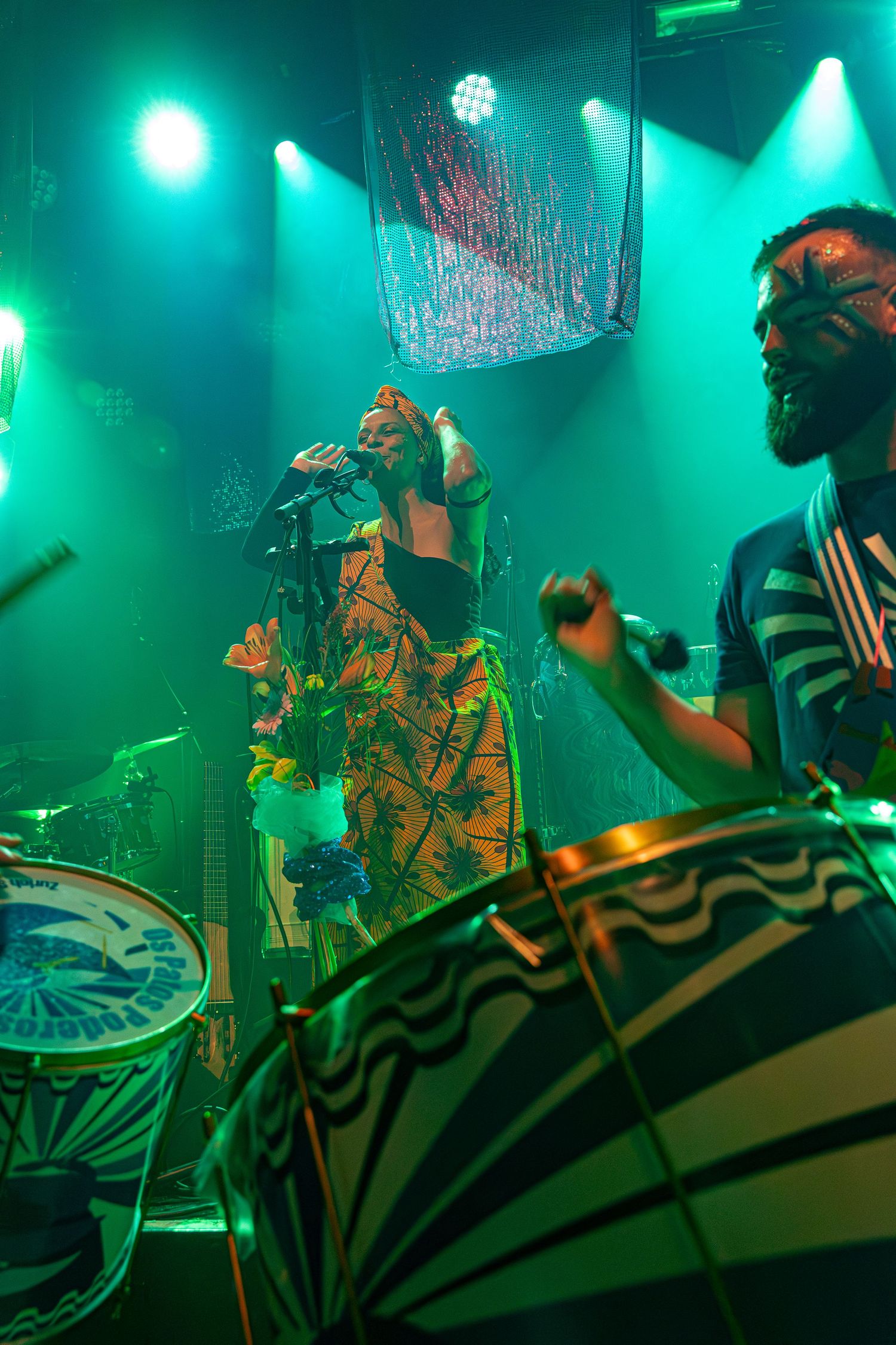 Concert performance with drummer and singer under dramatic green stage lighting.