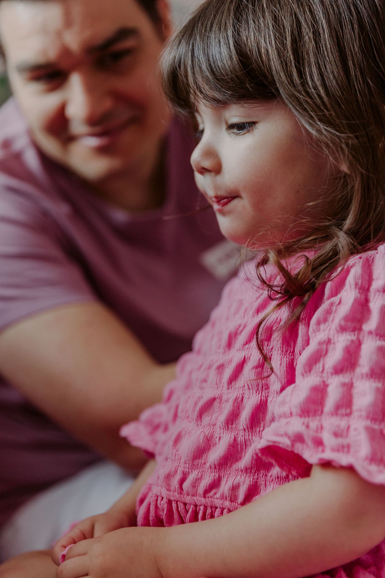 Intimate family moment captured in warm tones with pink clothing and soft natural lighting.