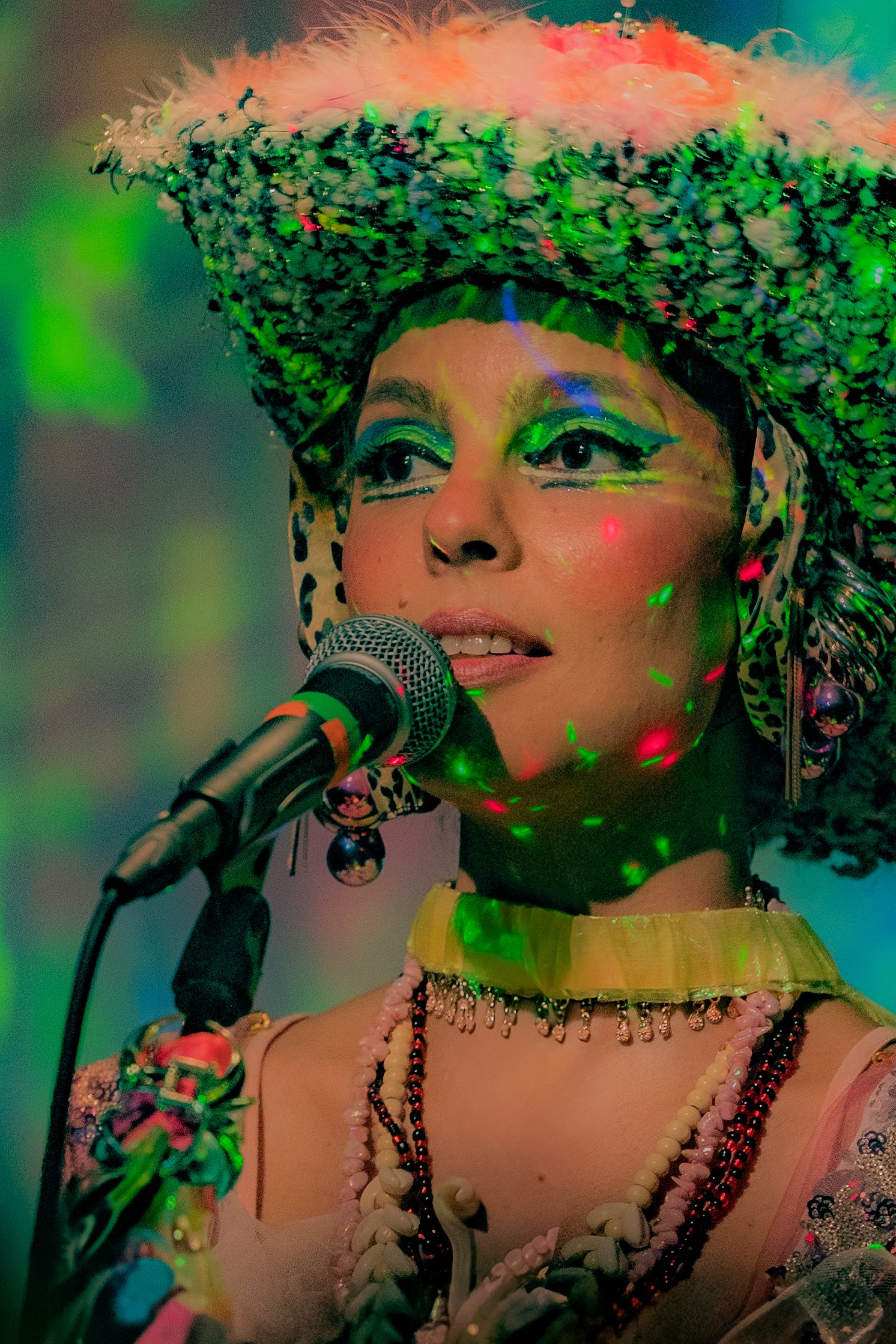 Colorful portrait of performer in elaborate headpiece singing into microphone.