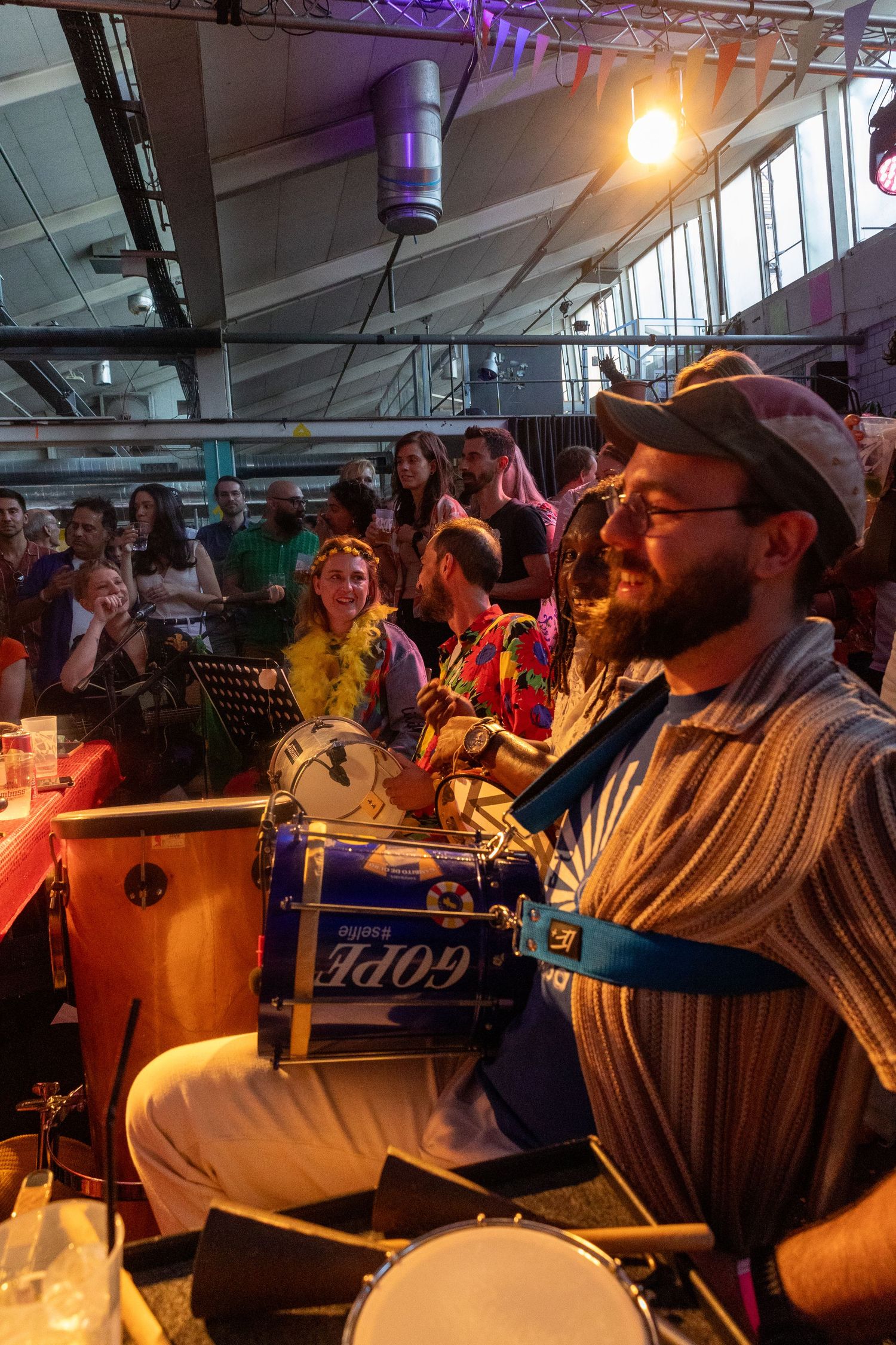 Musician playing drums at lively indoor celebration with crowd in background.