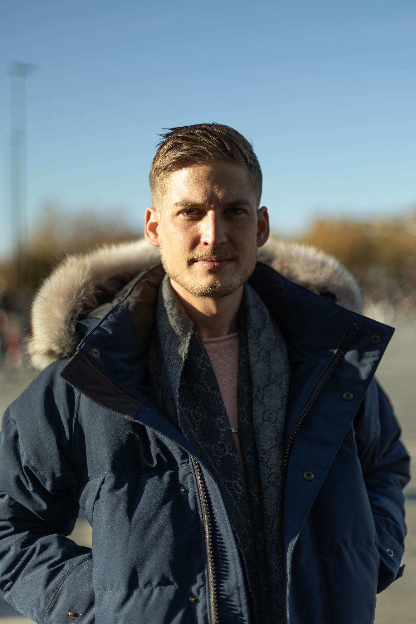 Portrait of person wearing navy puffer jacket with fur hood trim outdoors.