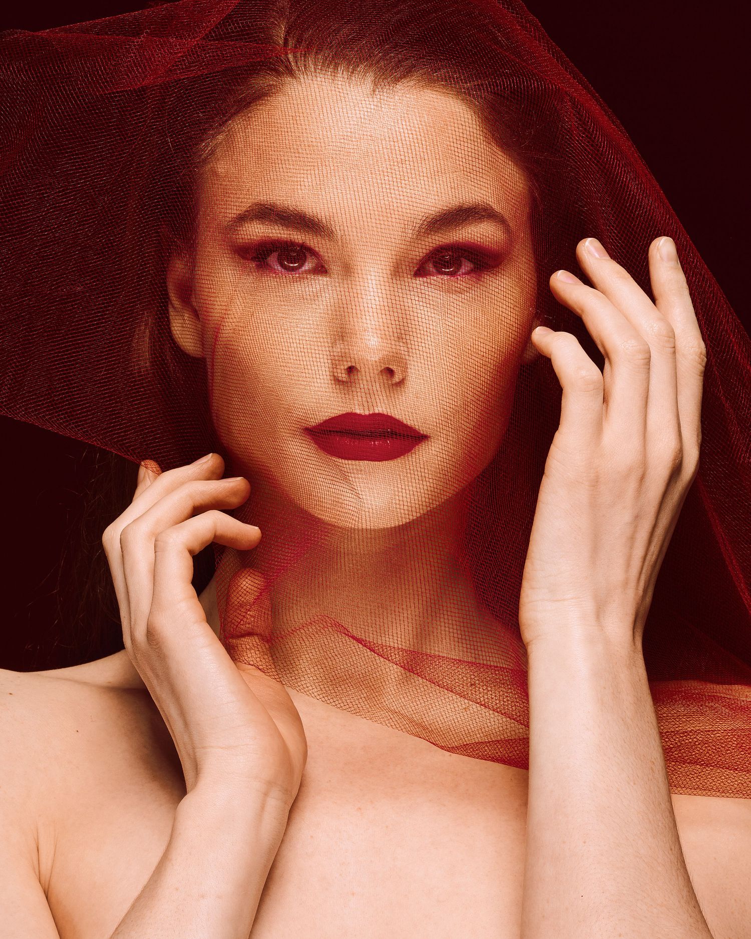 Glamour beauty shot with red tulle fabric and dramatic makeup against red backdrop.