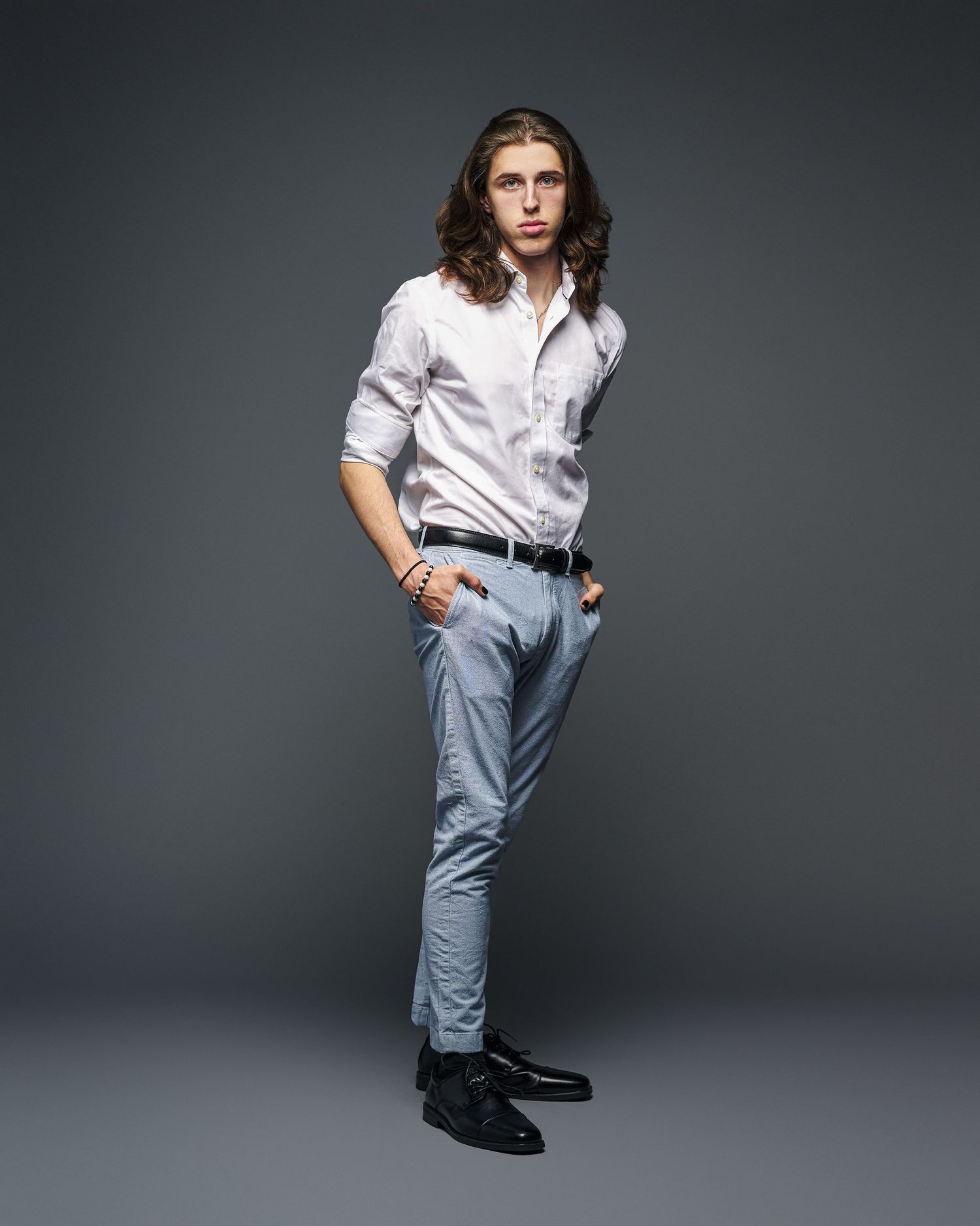 Fashion portrait of model in classic white shirt and light blue pants against dark backdrop.