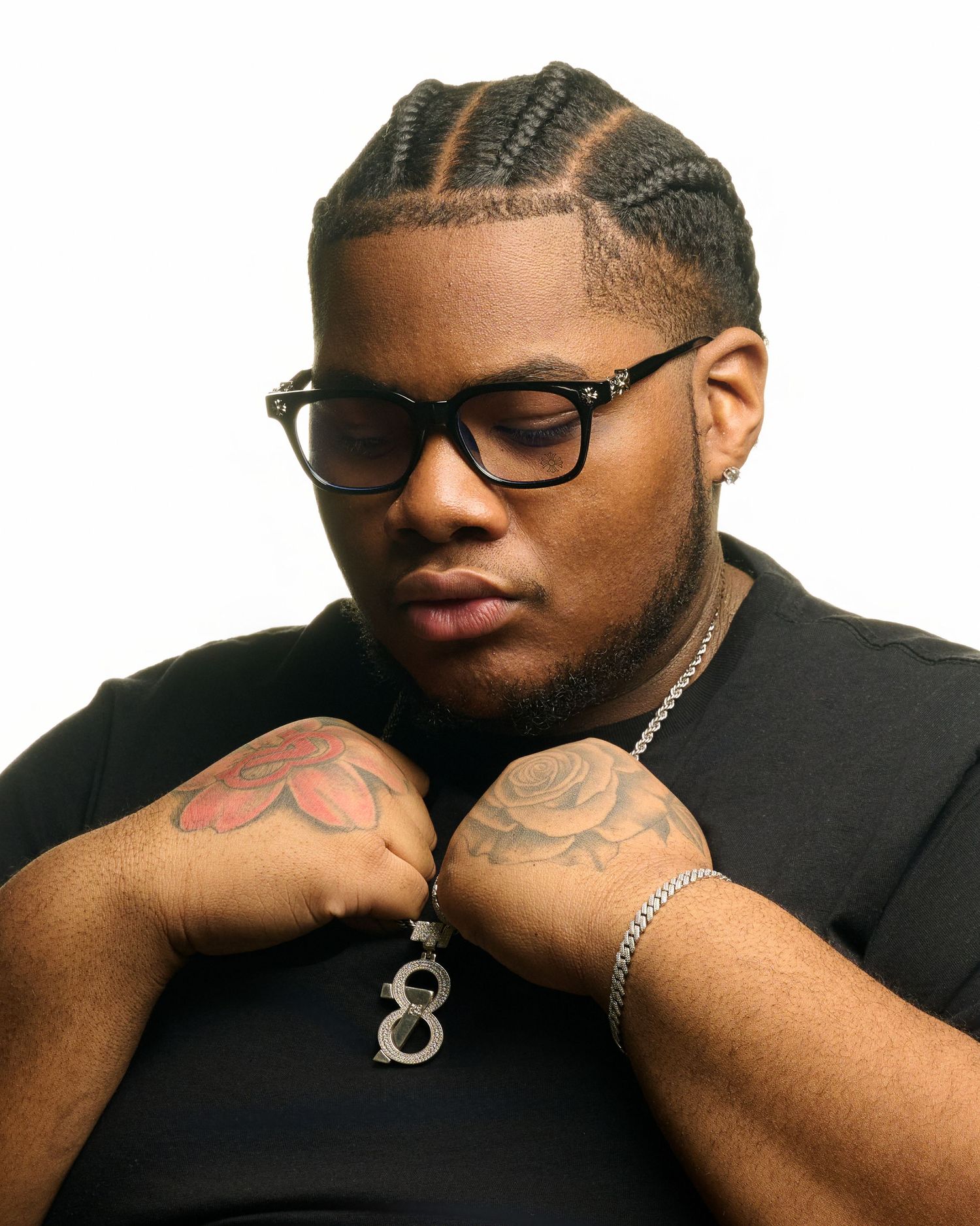 Studio portrait of person wearing glasses and black shirt with cornrow braids and tattoos.