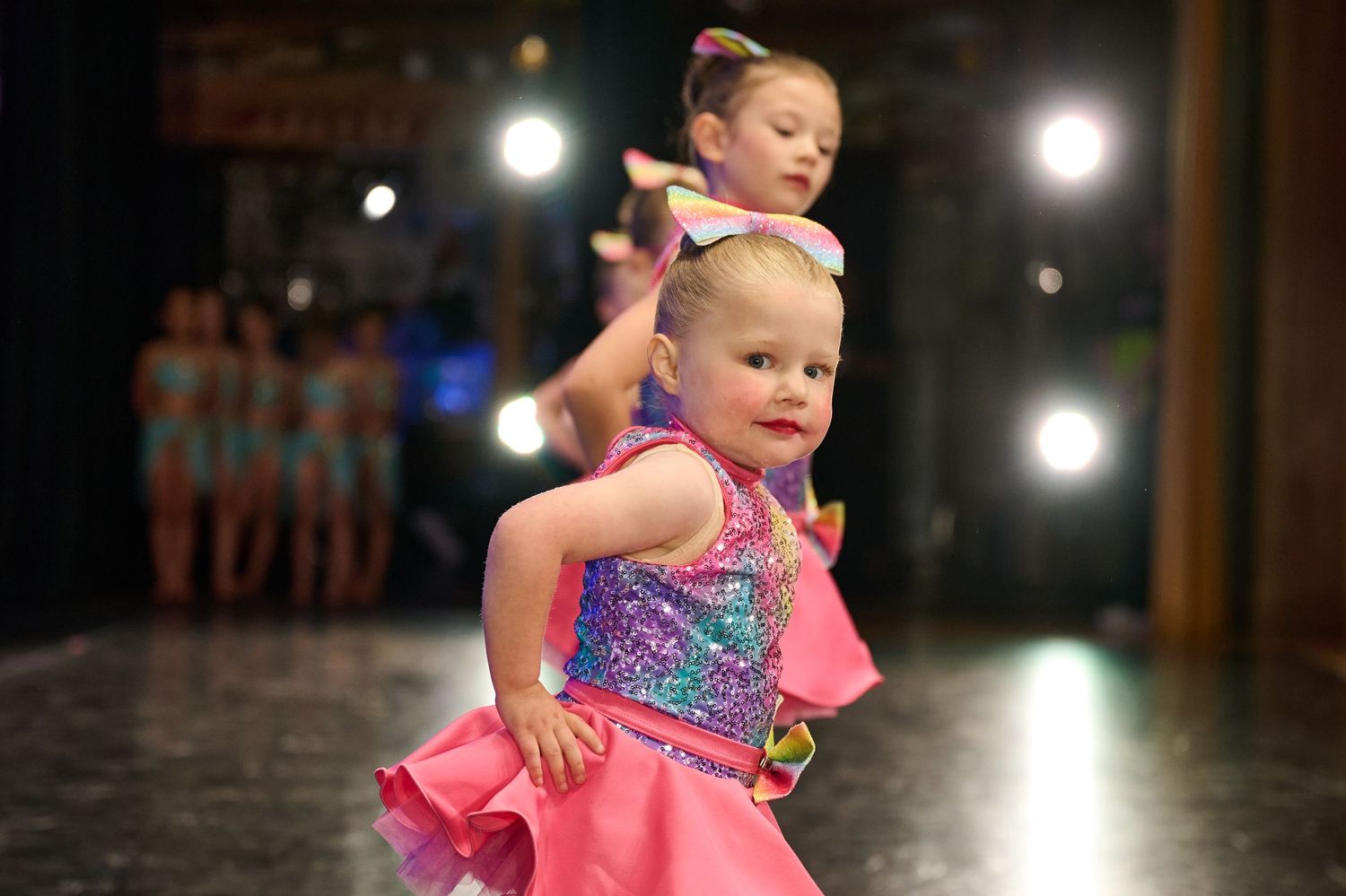 Young dancers in bright pink sequined costumes performing energetically on stage.