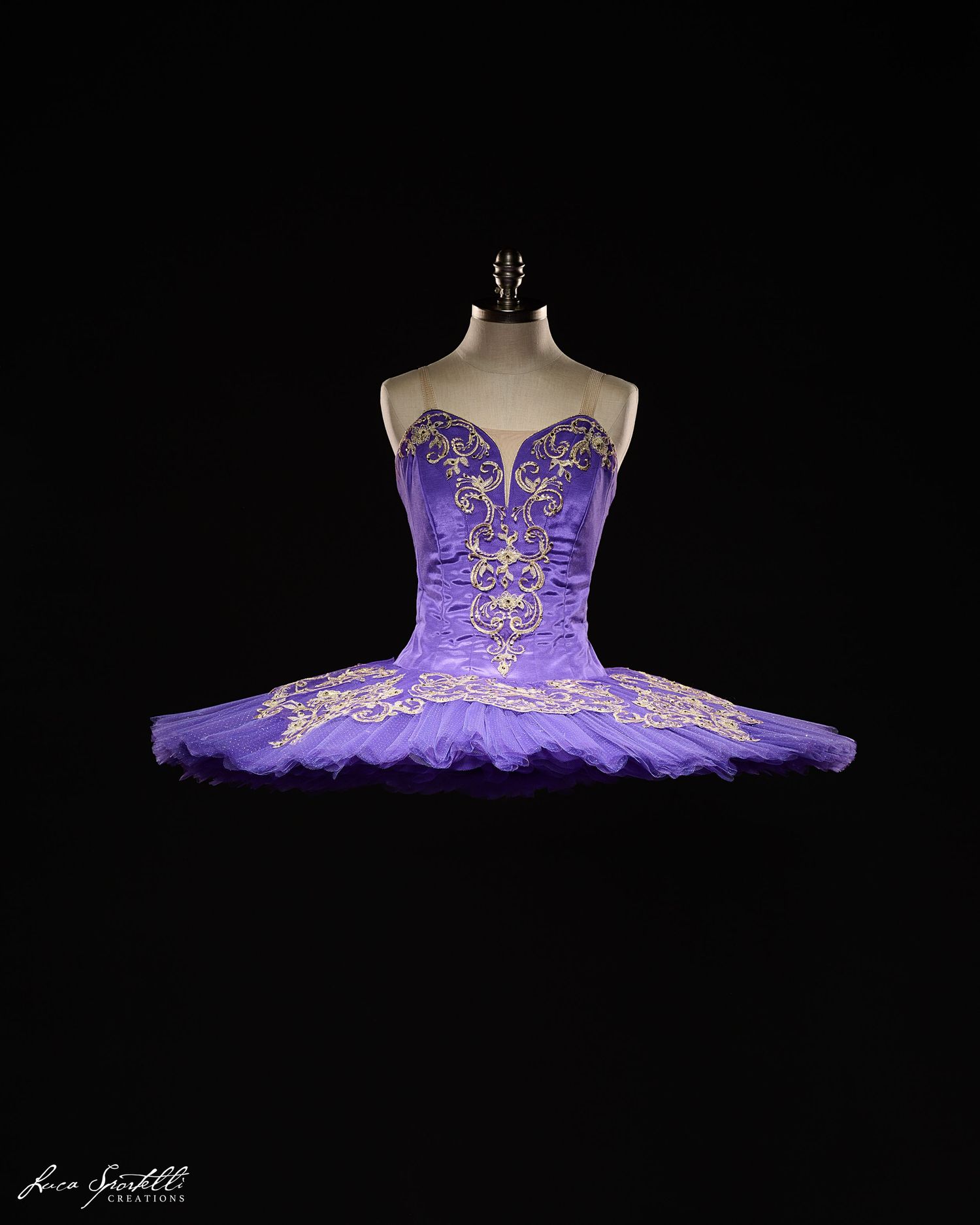 Purple and gold classical ballet tutu with ornate embellishments displayed on mannequin against black background.