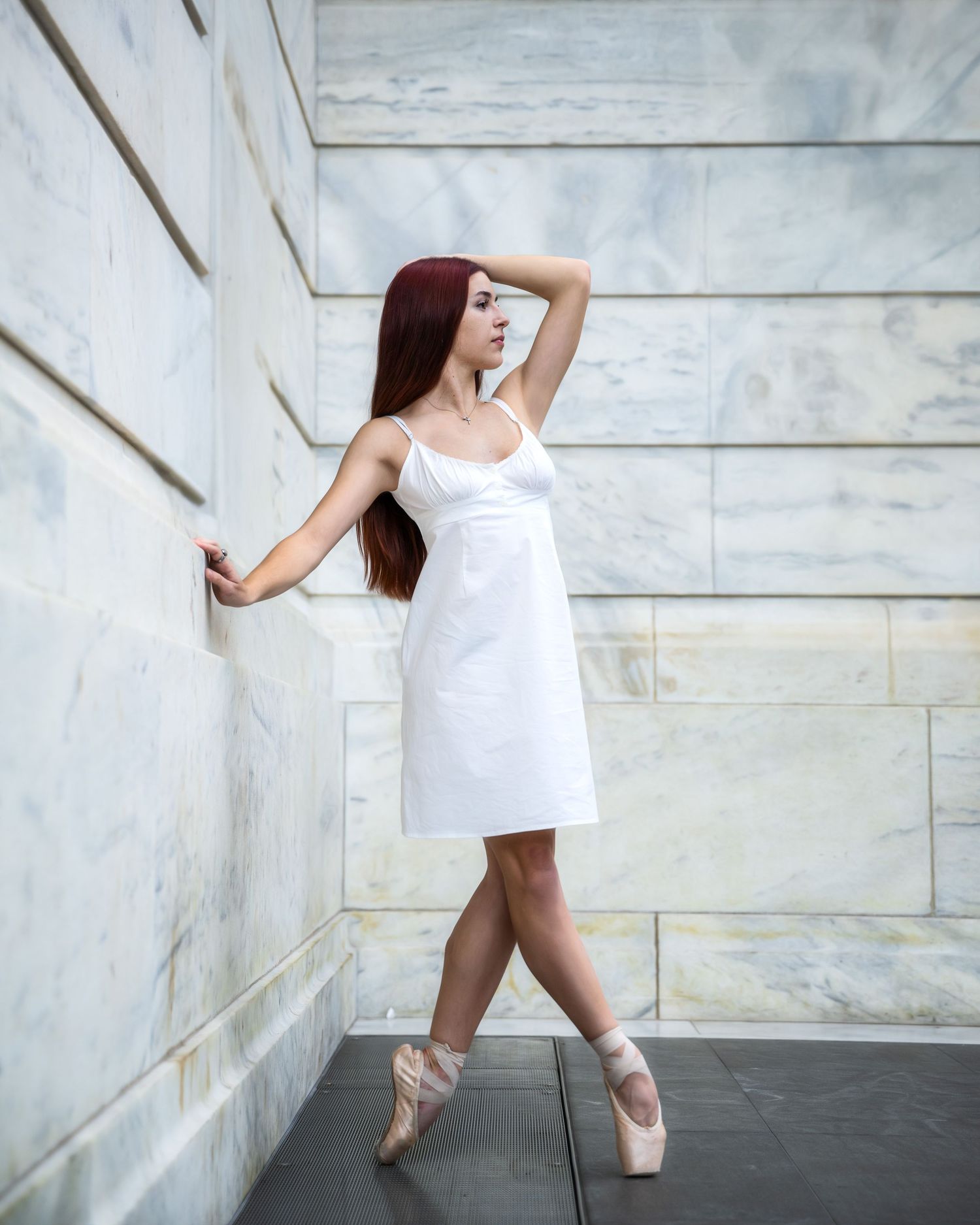 Ballet dancer in white dress poses gracefully against marble wall backdrop.