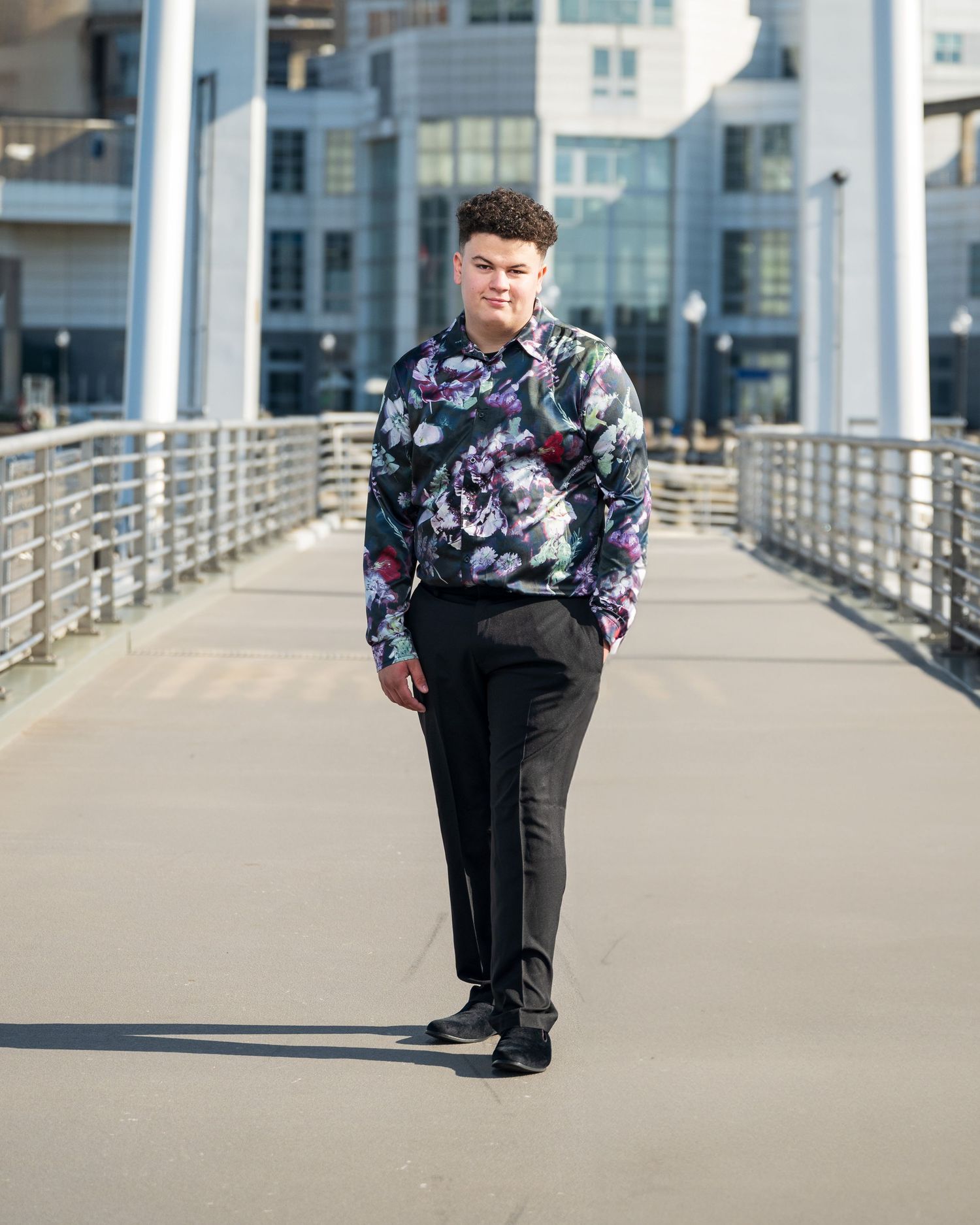 A modern urban portrait of someone in a patterned sweater walking along a contemporary bridge walkway.