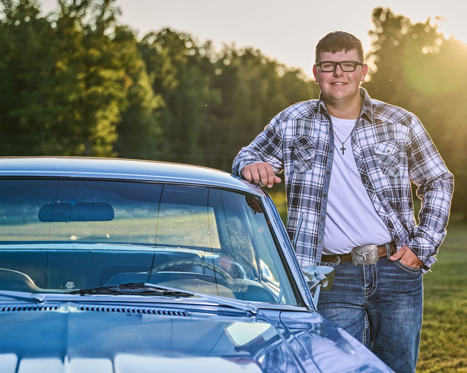A casual portrait of someone leaning against a classic blue car during golden hour in a park setting.