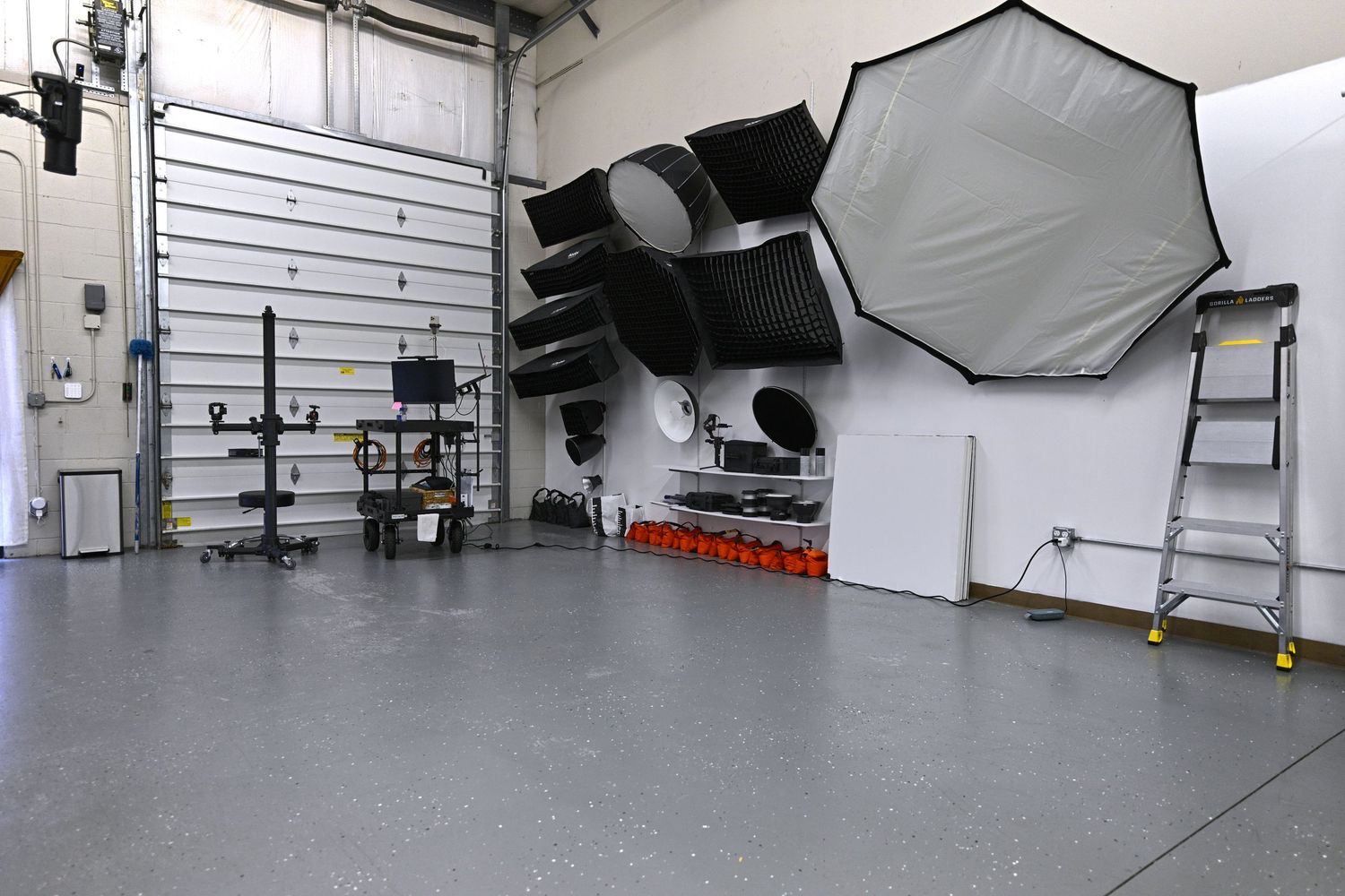 Professional photography studio setup with lighting equipment, umbrellas, and stands against white wall.