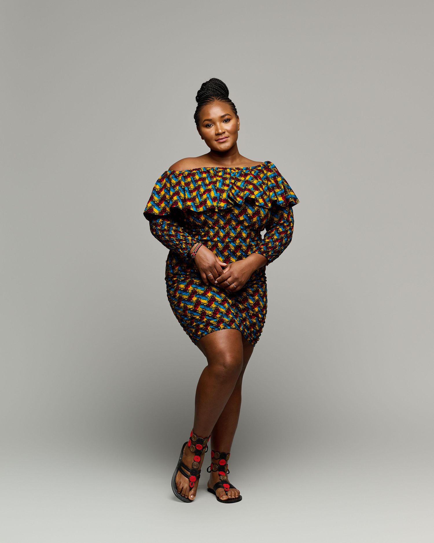 Model wearing patterned dress poses elegantly against grey backdrop.