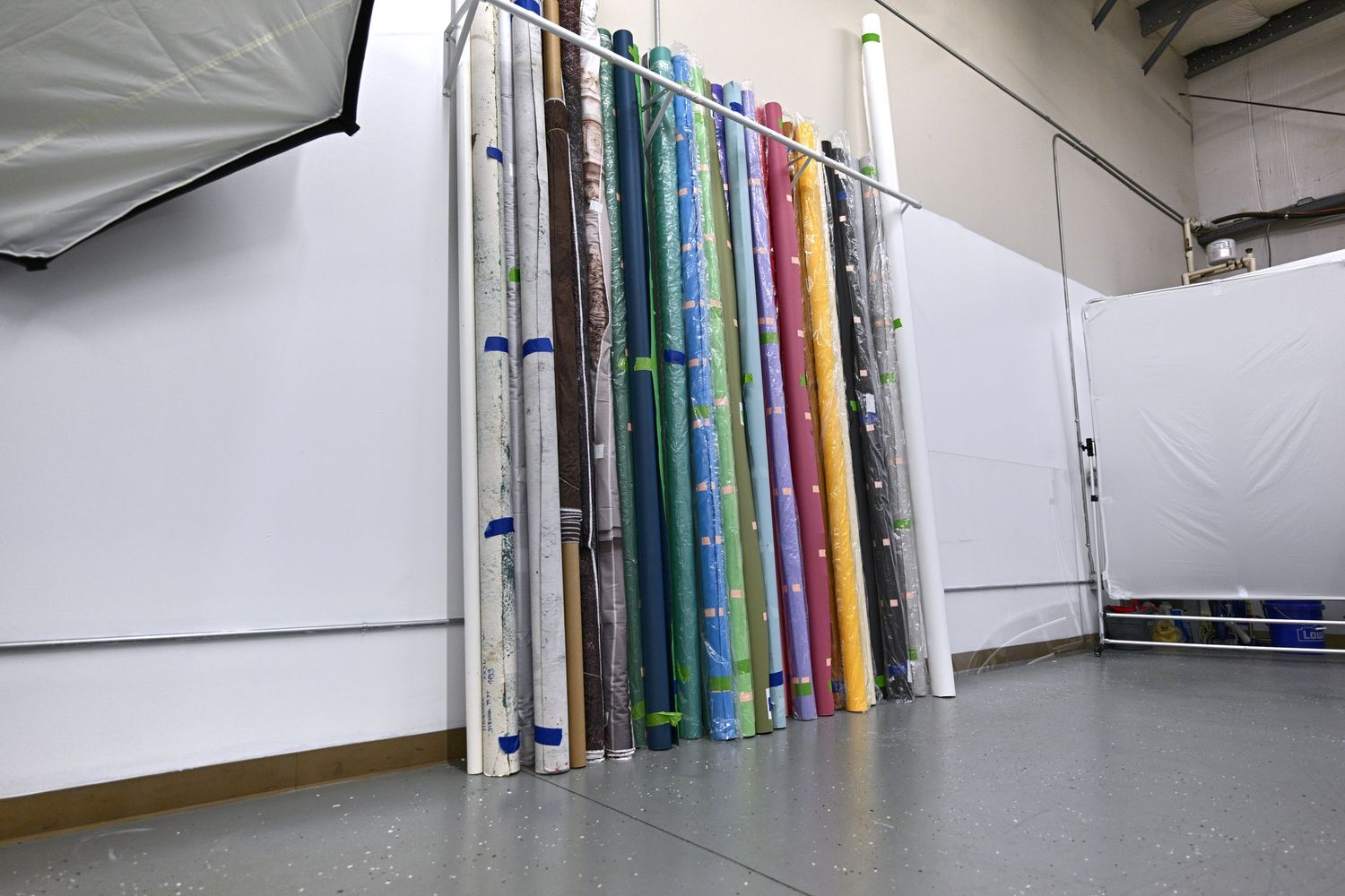Collection of colorful photography backdrop rolls stored against white studio wall.