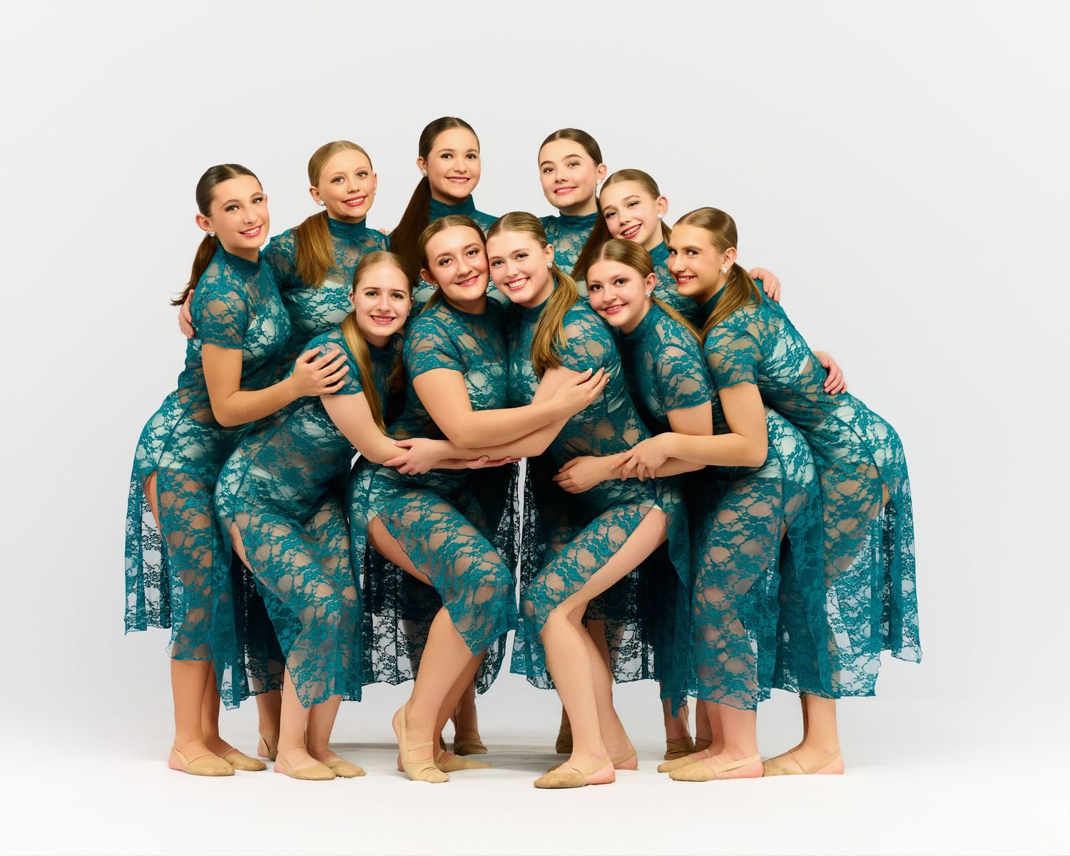 Dance ensemble wearing matching teal lace dresses in group portrait formation.