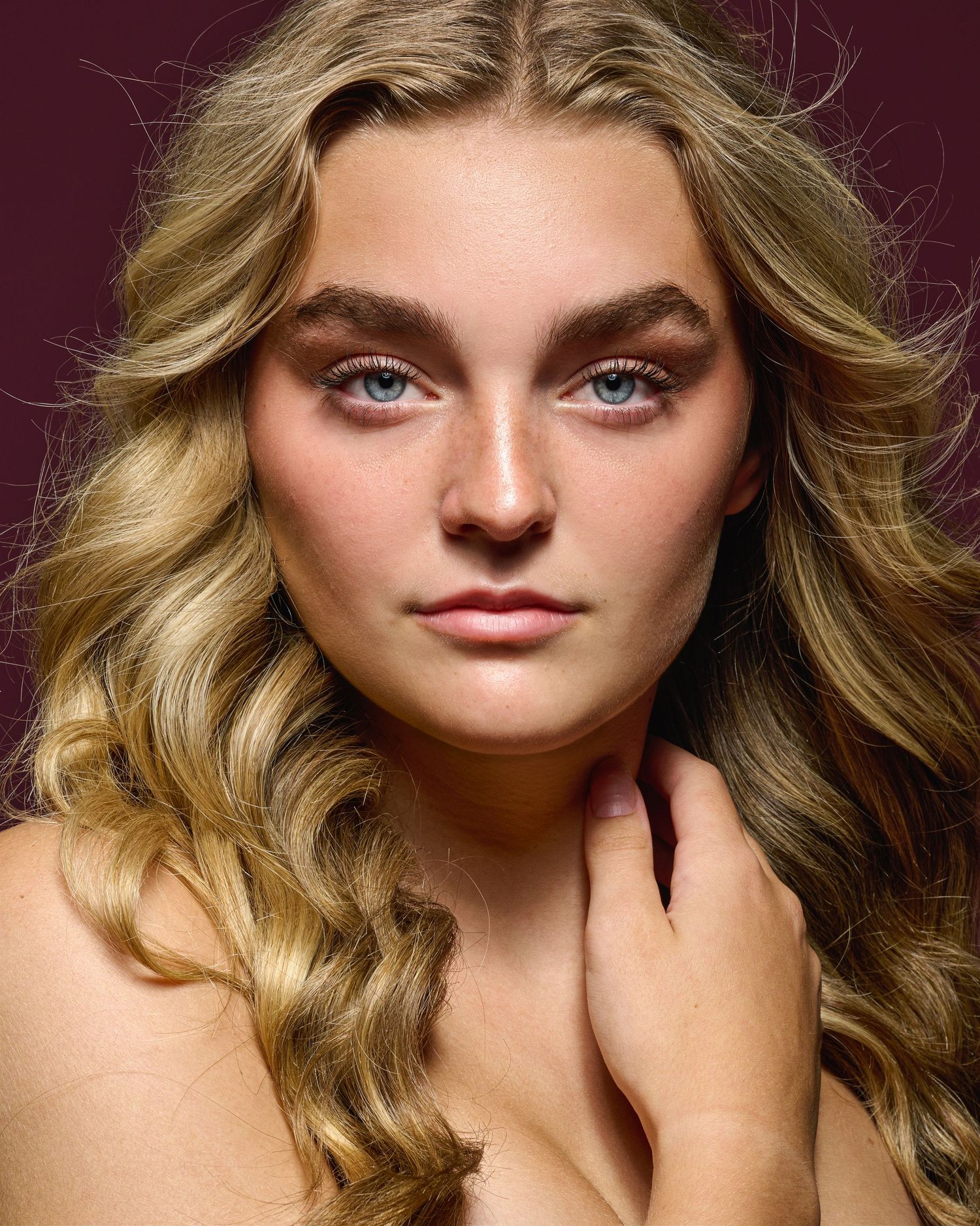 Close-up beauty portrait of a model with flowing blonde hair against dark background and dramatic lighting.