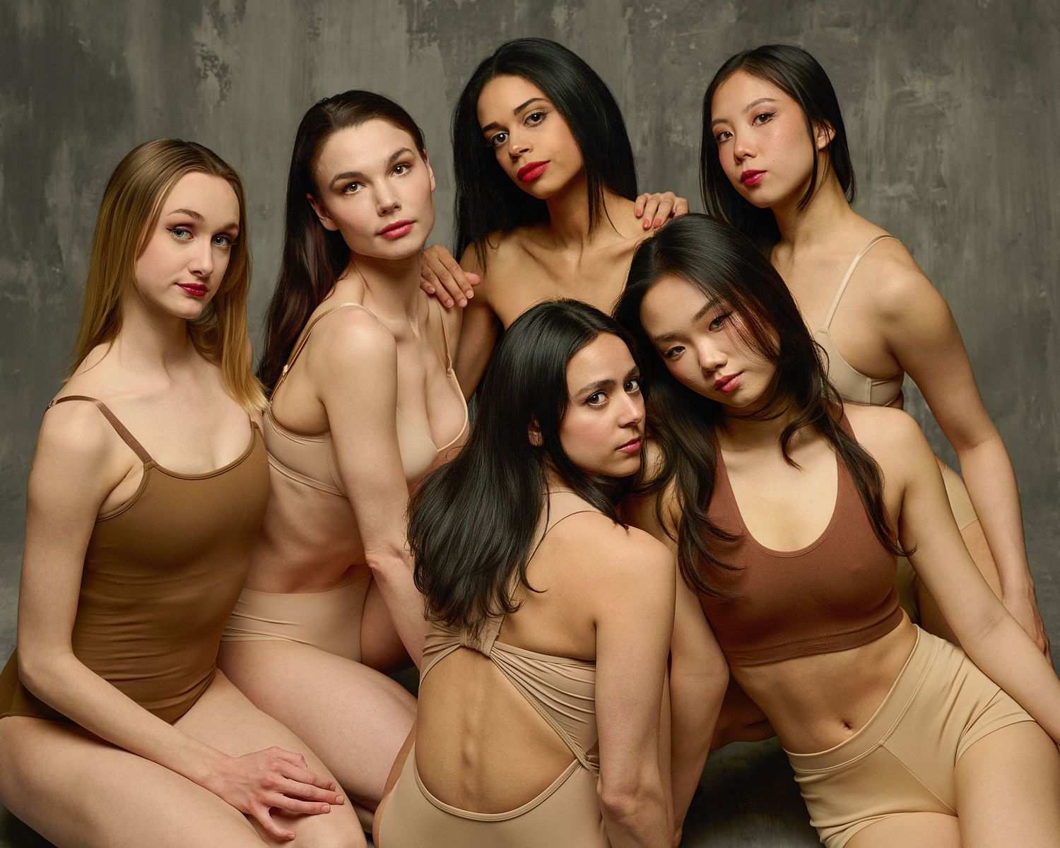 Artistic portrait of models wearing neutral-colored bodysuits against textured background.