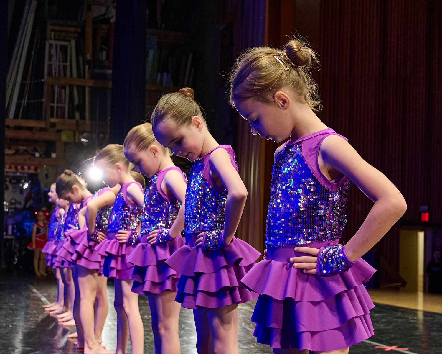 Young dancers in sparkly purple costumes lined up on stage during recital performance.
