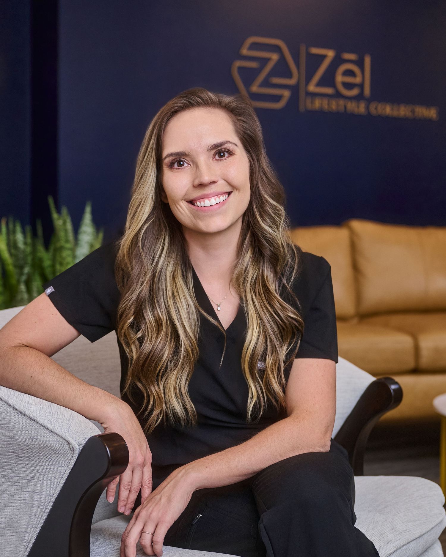 Healthcare provider in black scrubs seated in professional office setting with branded wall background.