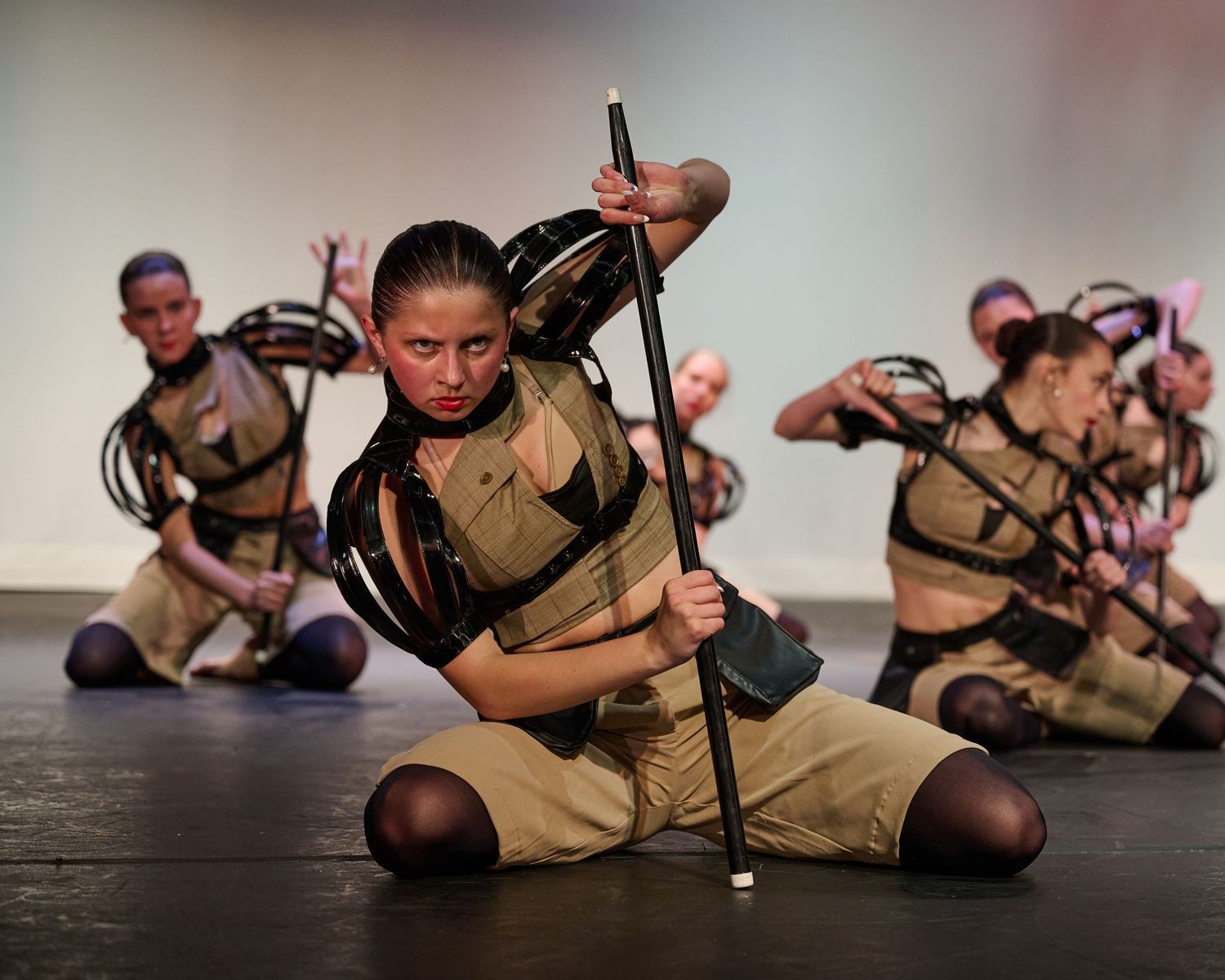 Dancers in military-inspired costumes perform an intense theatrical number with staffs on stage.