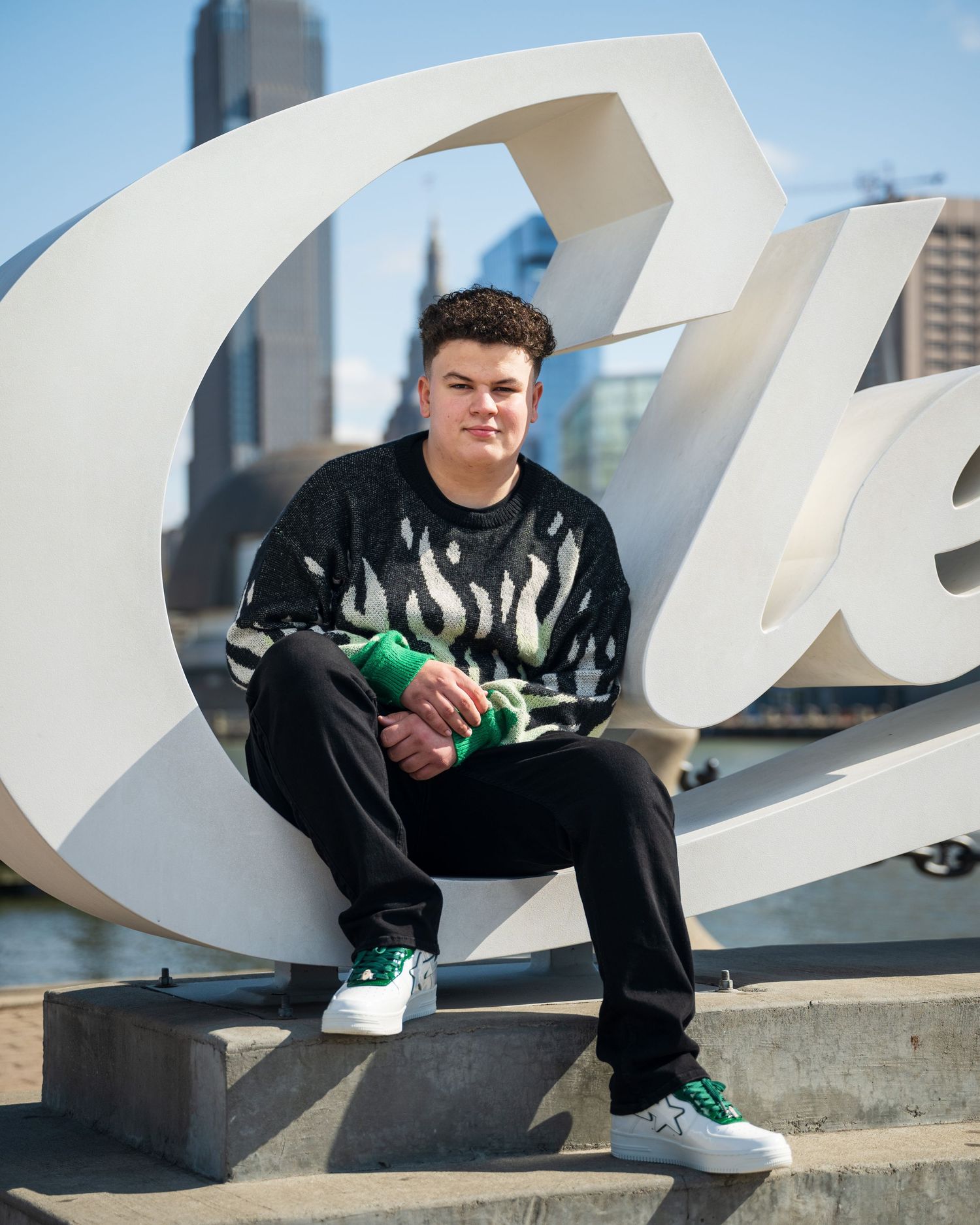 A stylish urban portrait featuring someone in streetwear sitting on a large white sculptural installation.