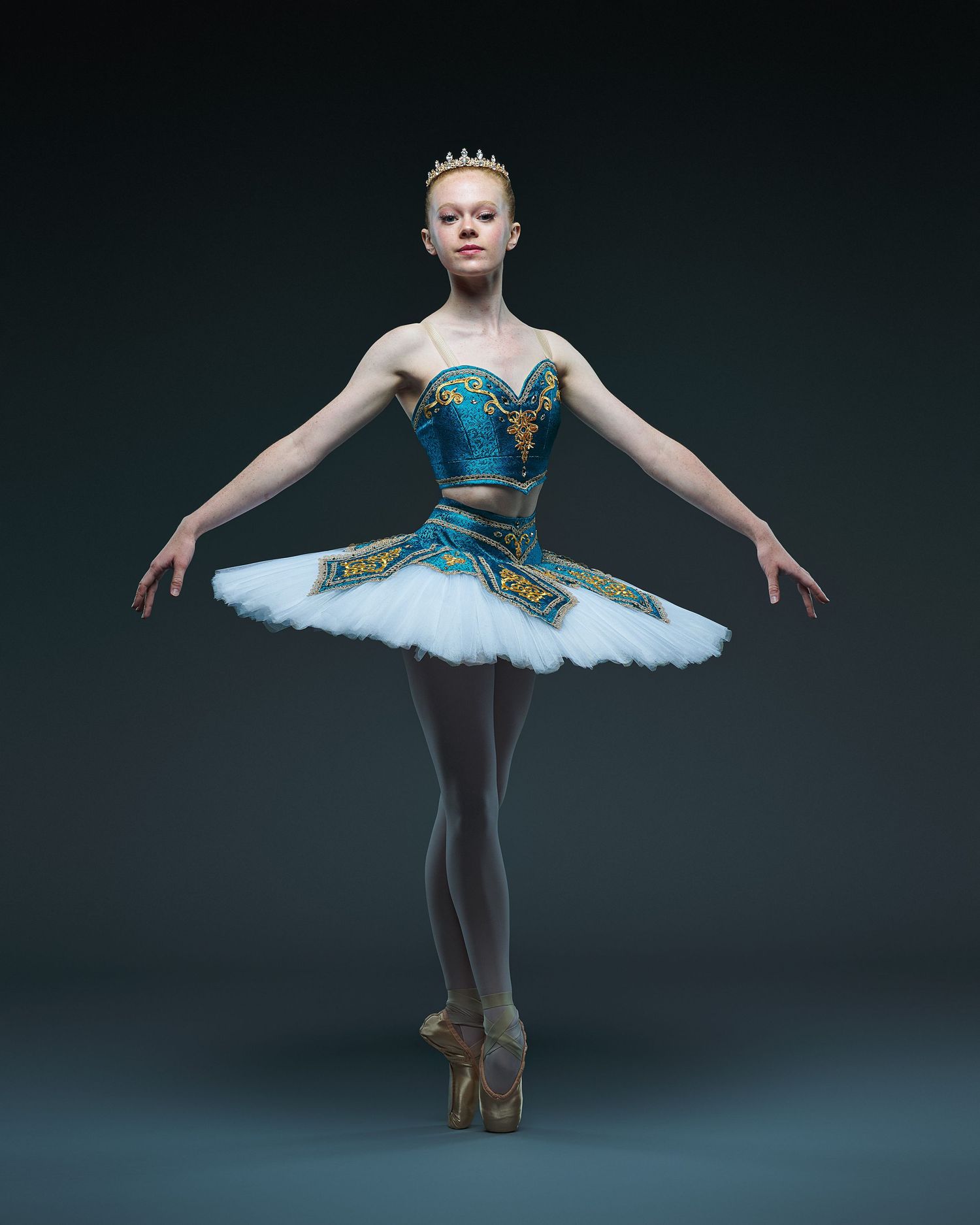 Dancer poses en pointe wearing turquoise and white classical tutu with ornate details.