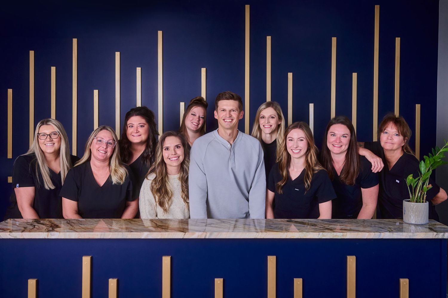 Group photo of healthcare staff in dark attire against blue wall with vertical wooden accent features.