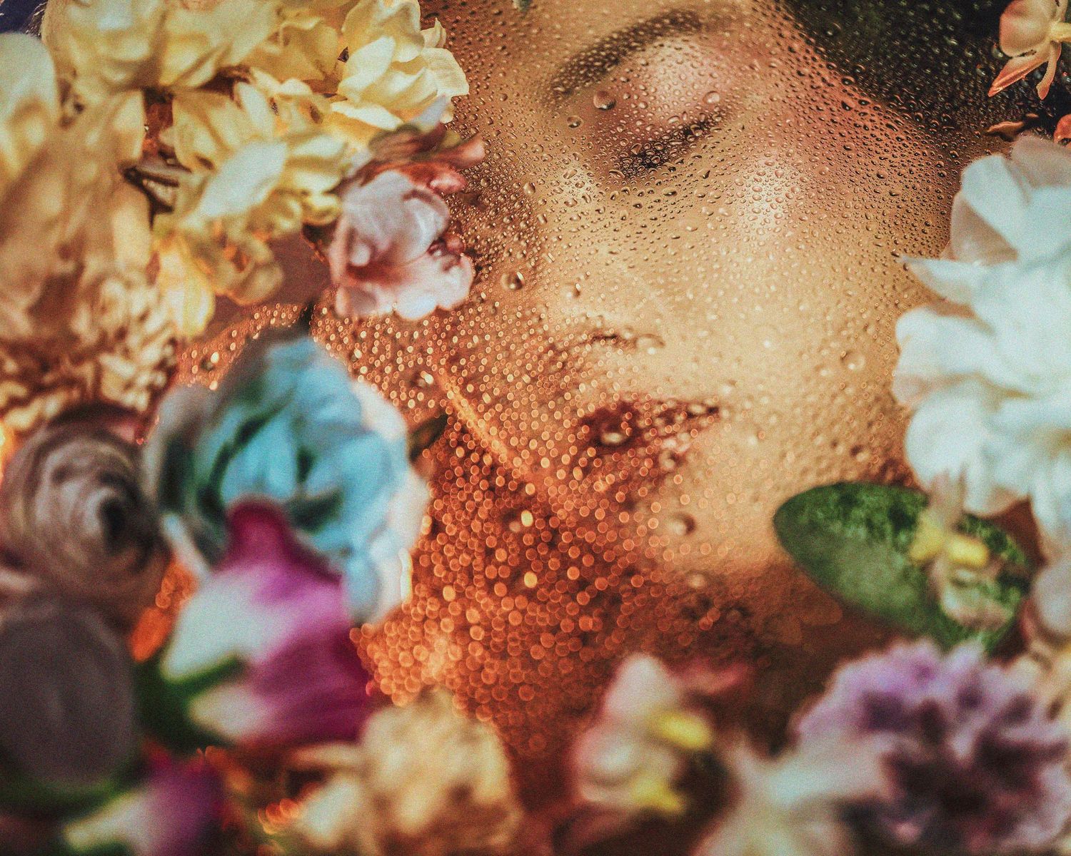 Artistic portrait featuring water droplets on skin with colorful flowers in warm lighting.