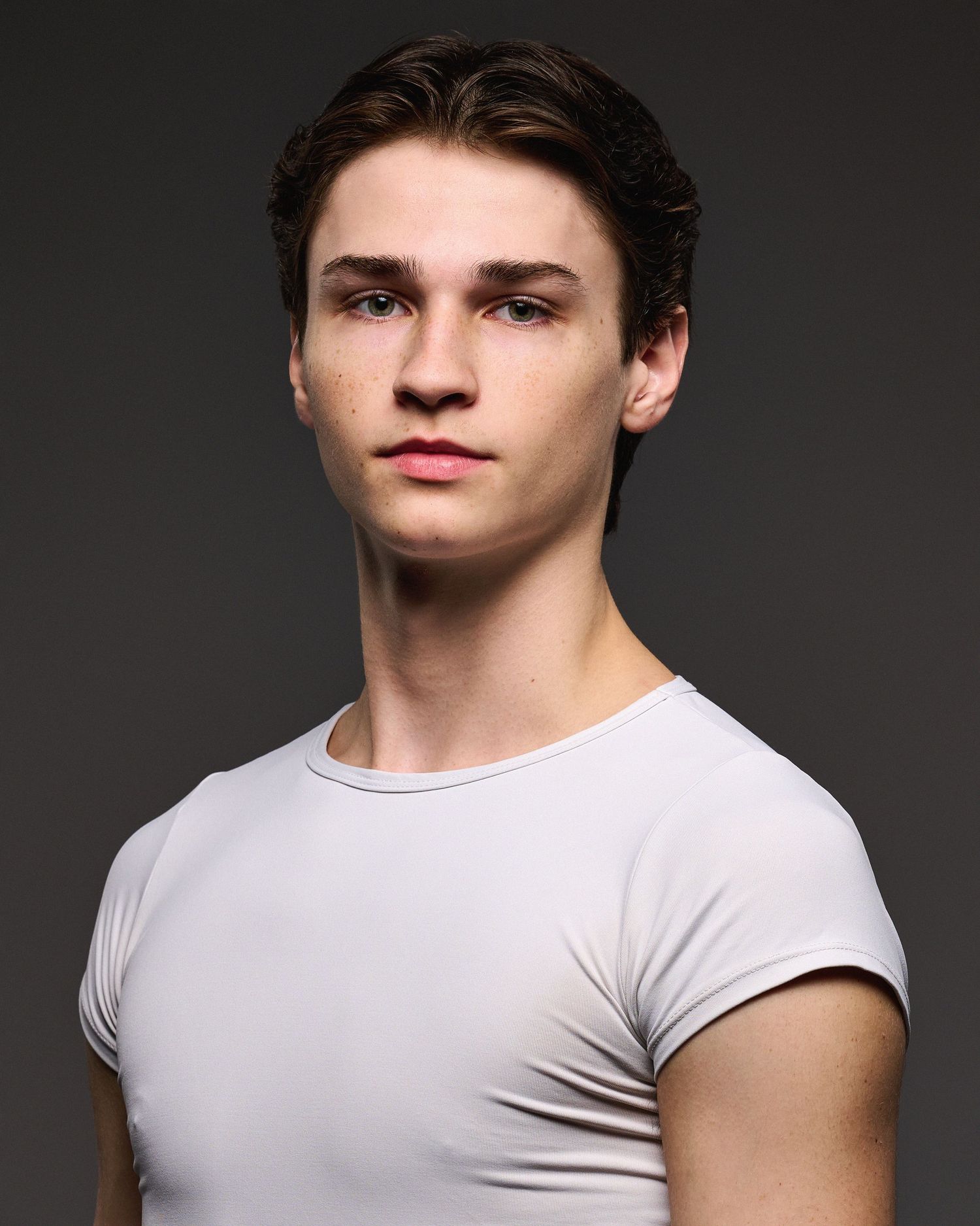 Professional dancer in white t-shirt poses against dark background for headshot portrait.