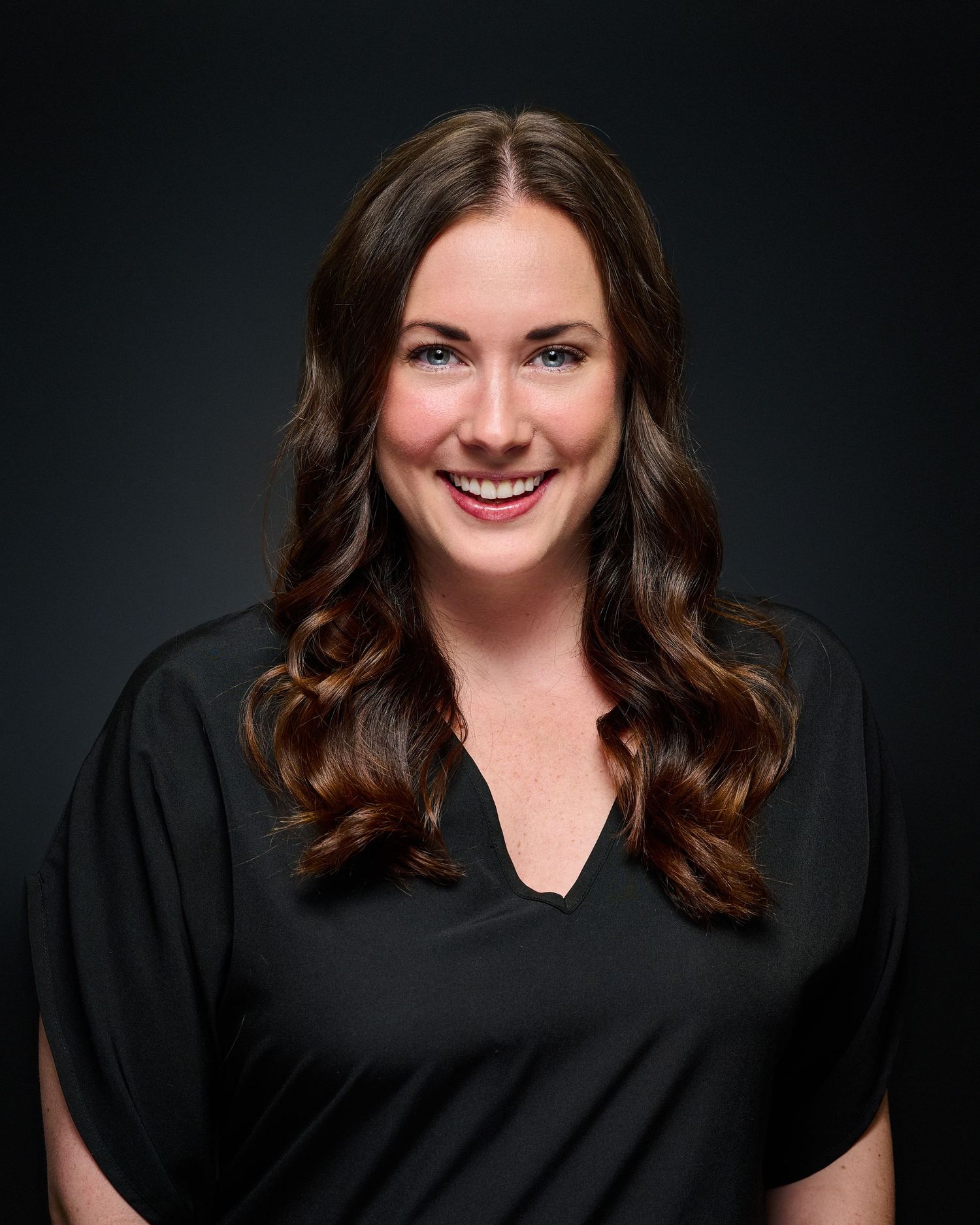 Professional headshot of a person in black attire against dark background.