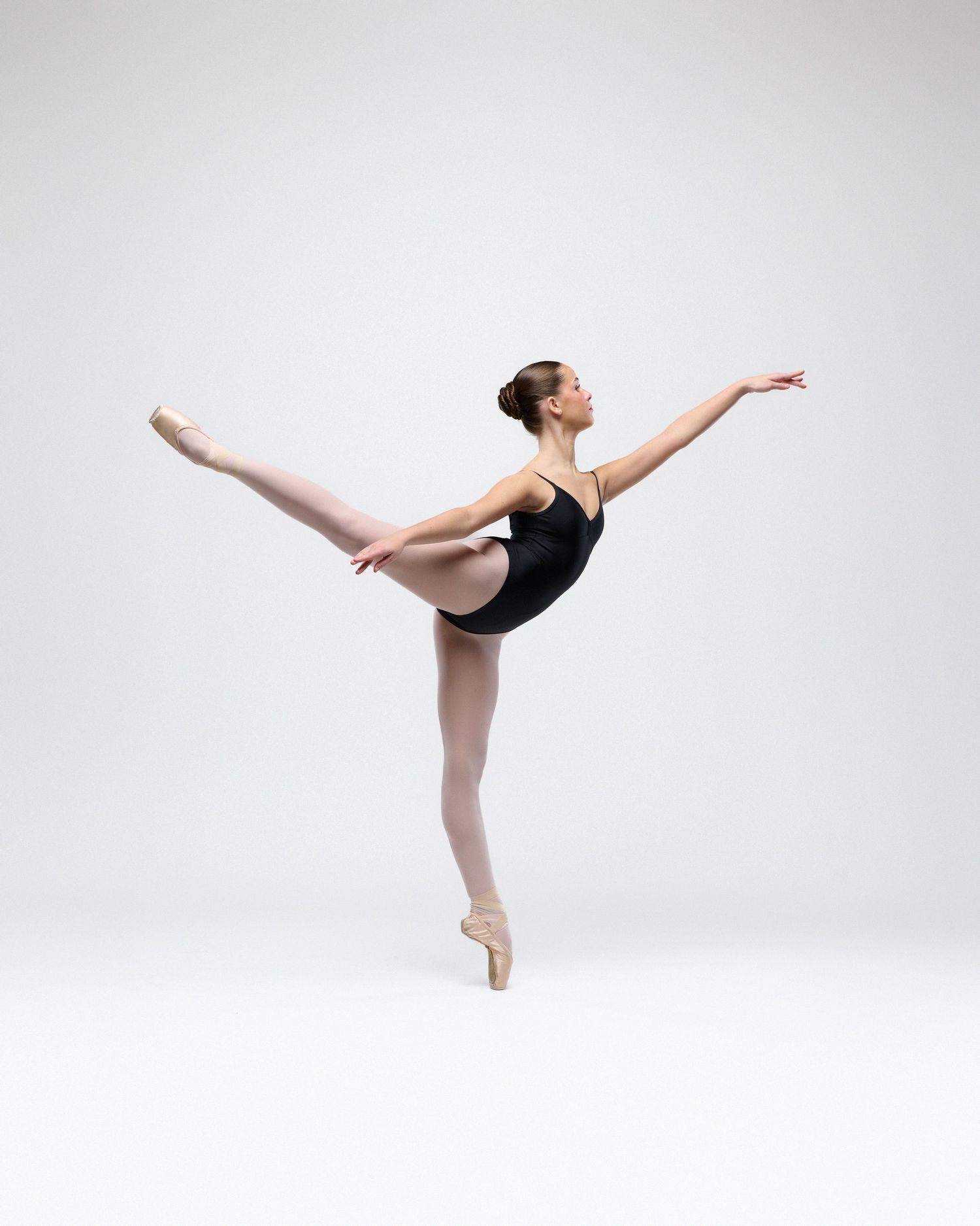 A ballet dancer in a black leotard performs an elegant arabesque pose on pointe.