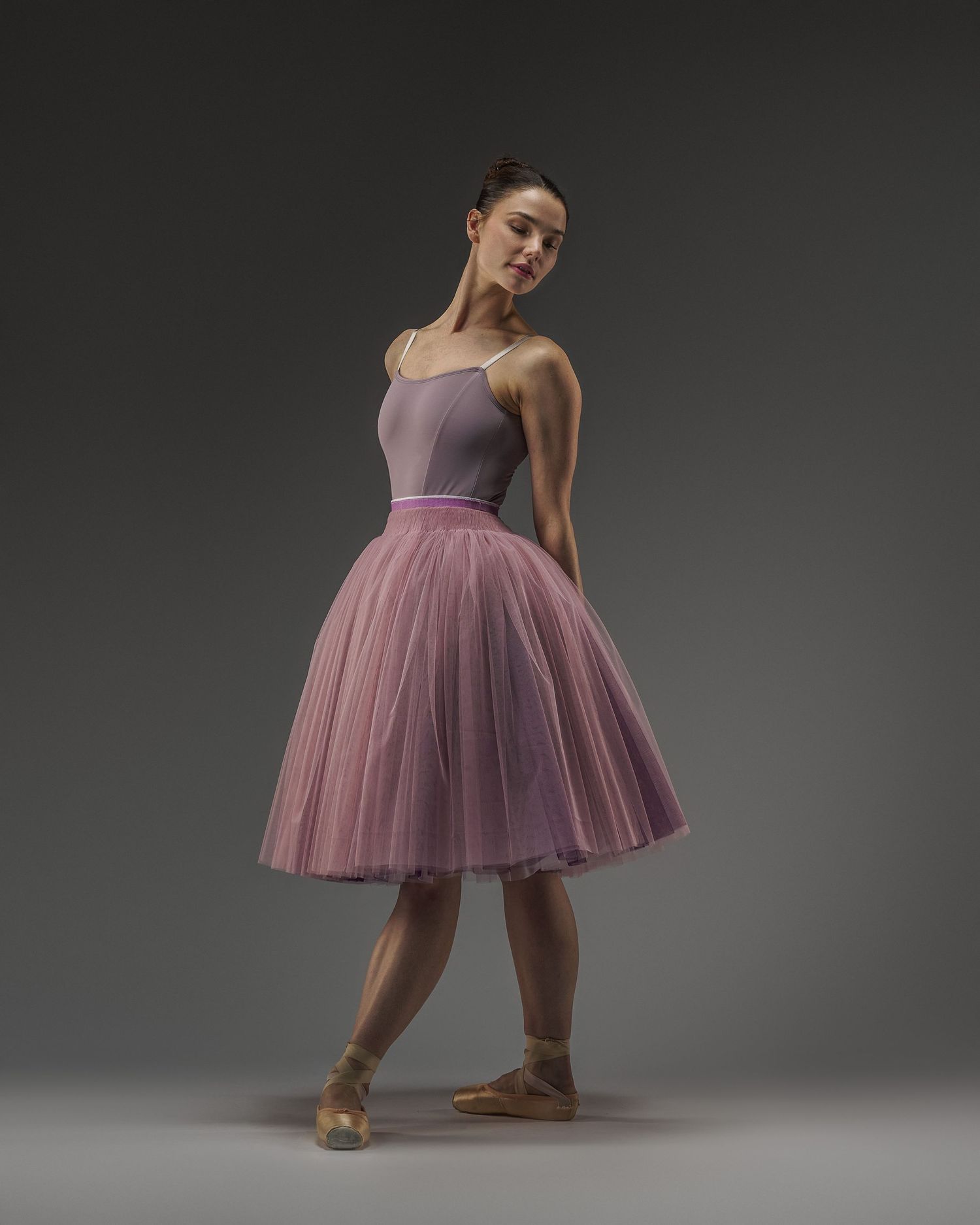 Ballerina in lavender leotard and pink tulle skirt poses gracefully in studio lighting.