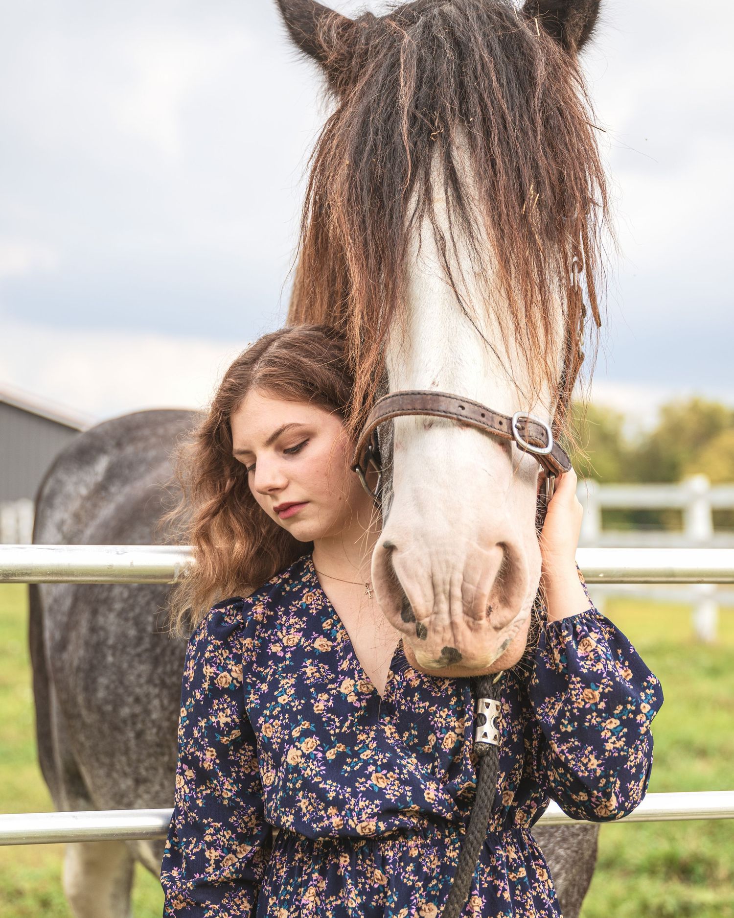 Close-up of brown and white horse with person in floral dress at stable.