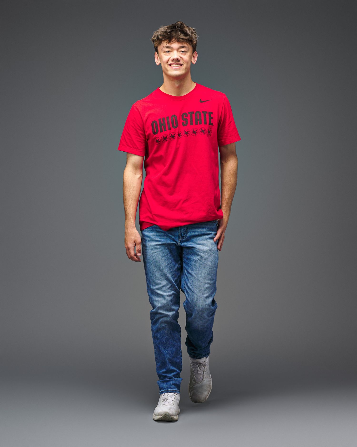Student in Ohio State University t-shirt walking against gray studio backdrop.