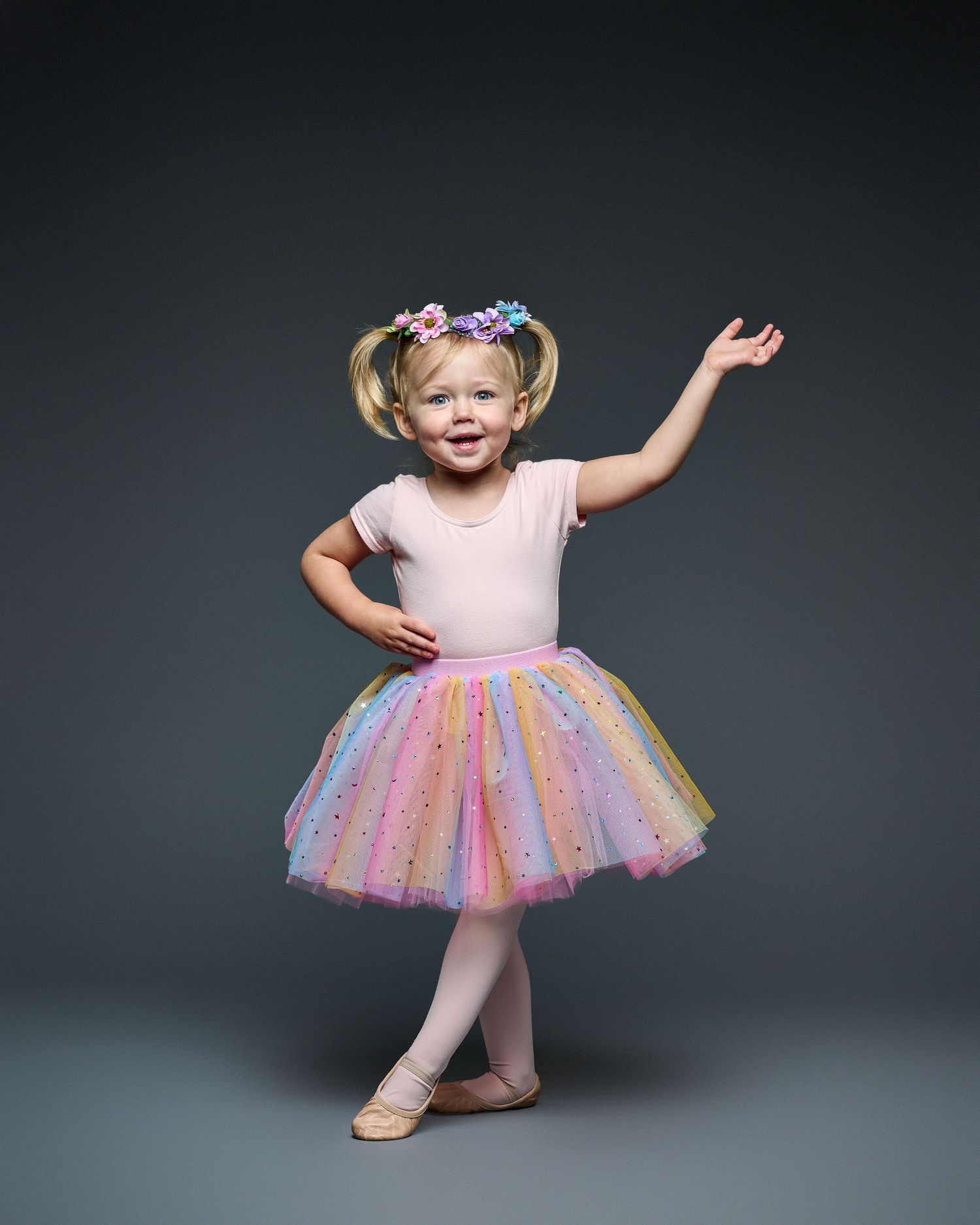 Small dancer strikes joyful pose in sparkly pastel tutu and ballet slippers.