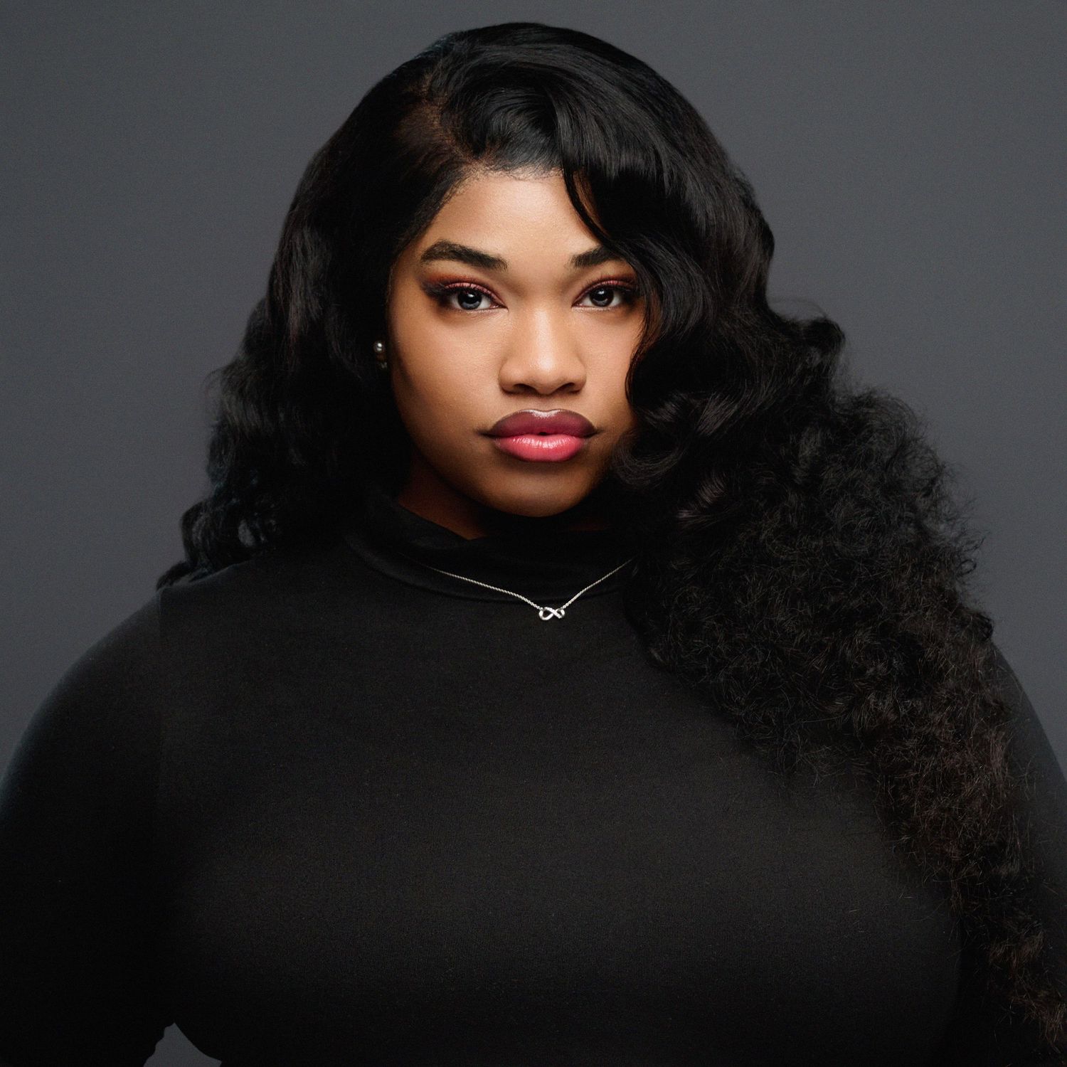 Studio portrait featuring long wavy black hair and black top against dark background.